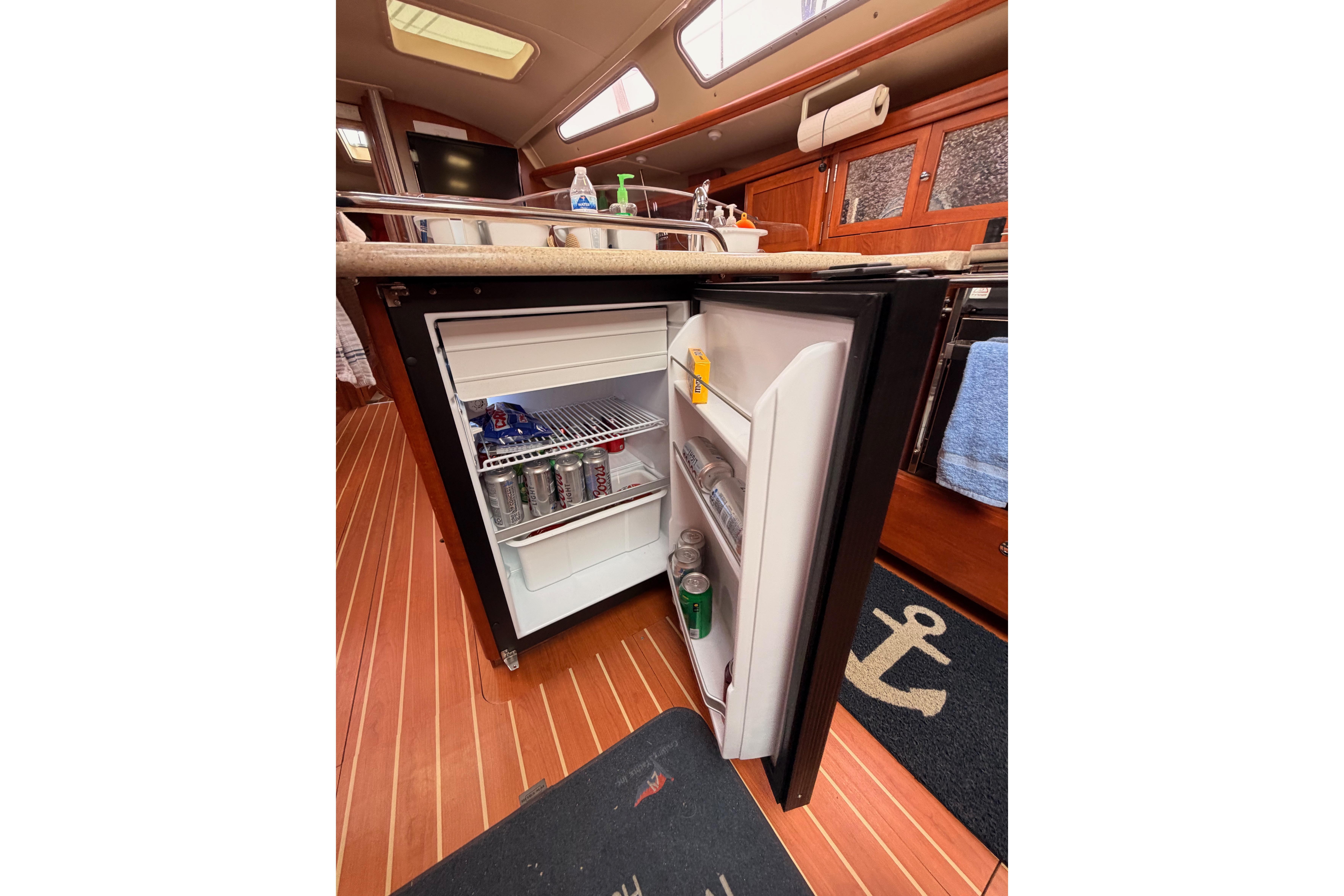 Open mini fridge in 2009 Hunter 38 yacht interior, showcasing beverages and snacks.