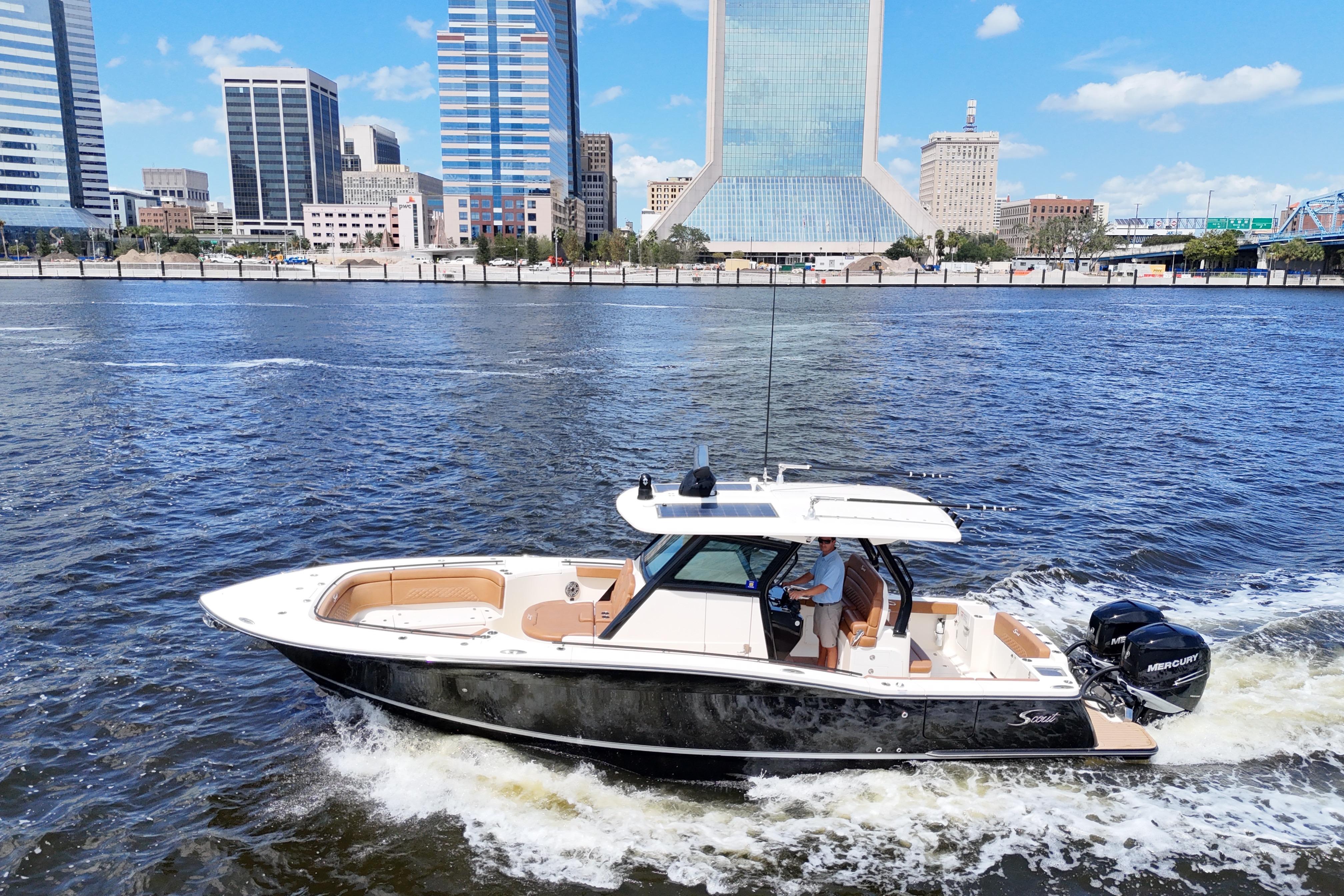 2021 Scout 330 LXF boat cruising on a river with city skyline backdrop.