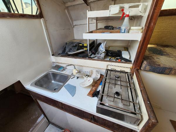 1985 Crowther Buccaneer boat kitchen with sink, stove, and storage shelves.