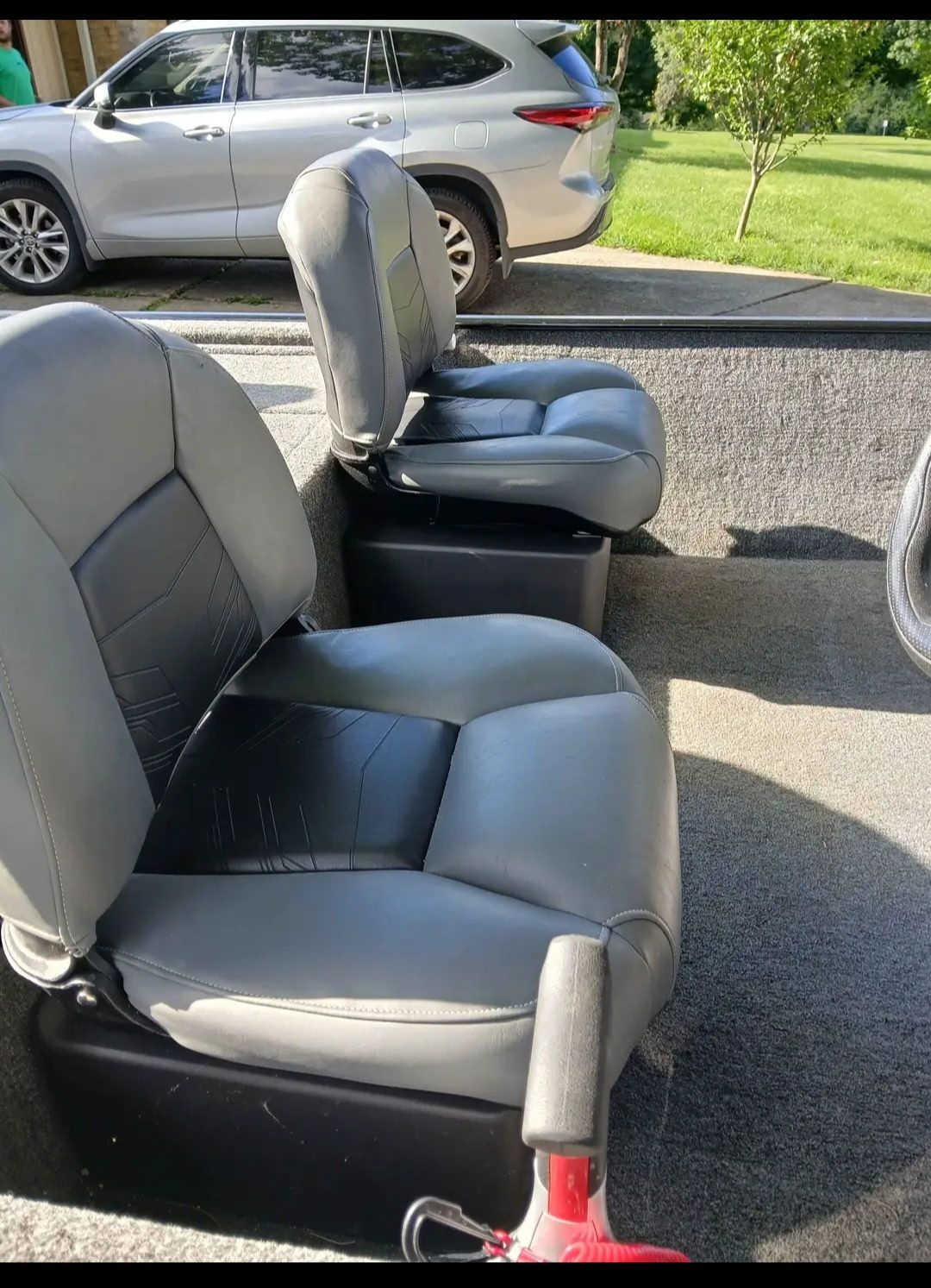 Two gray seats in a boat, with a car in the background on a driveway.