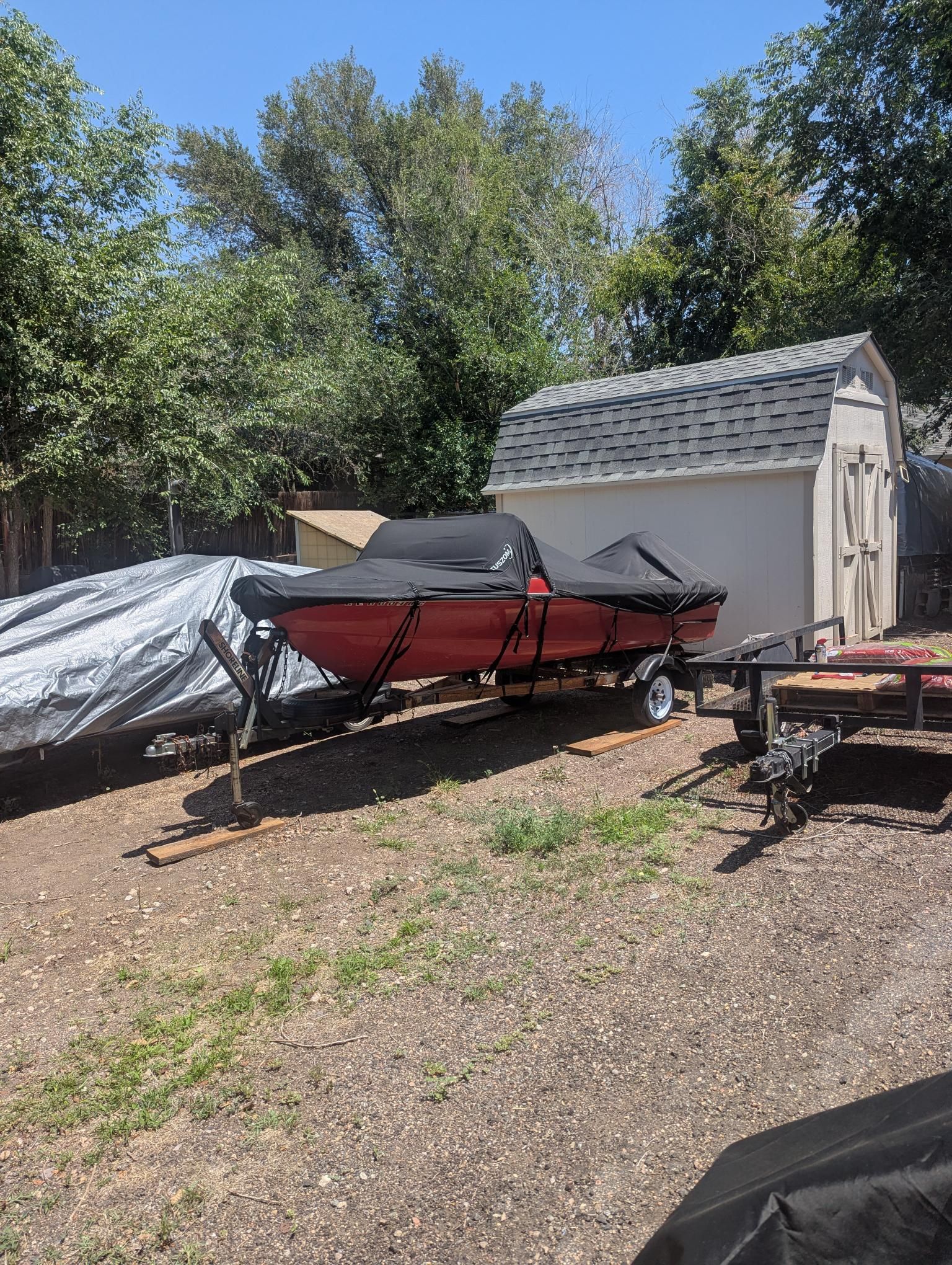 A red 1972 14' Swiss Craft runabout sits on a trailer next to a shed.