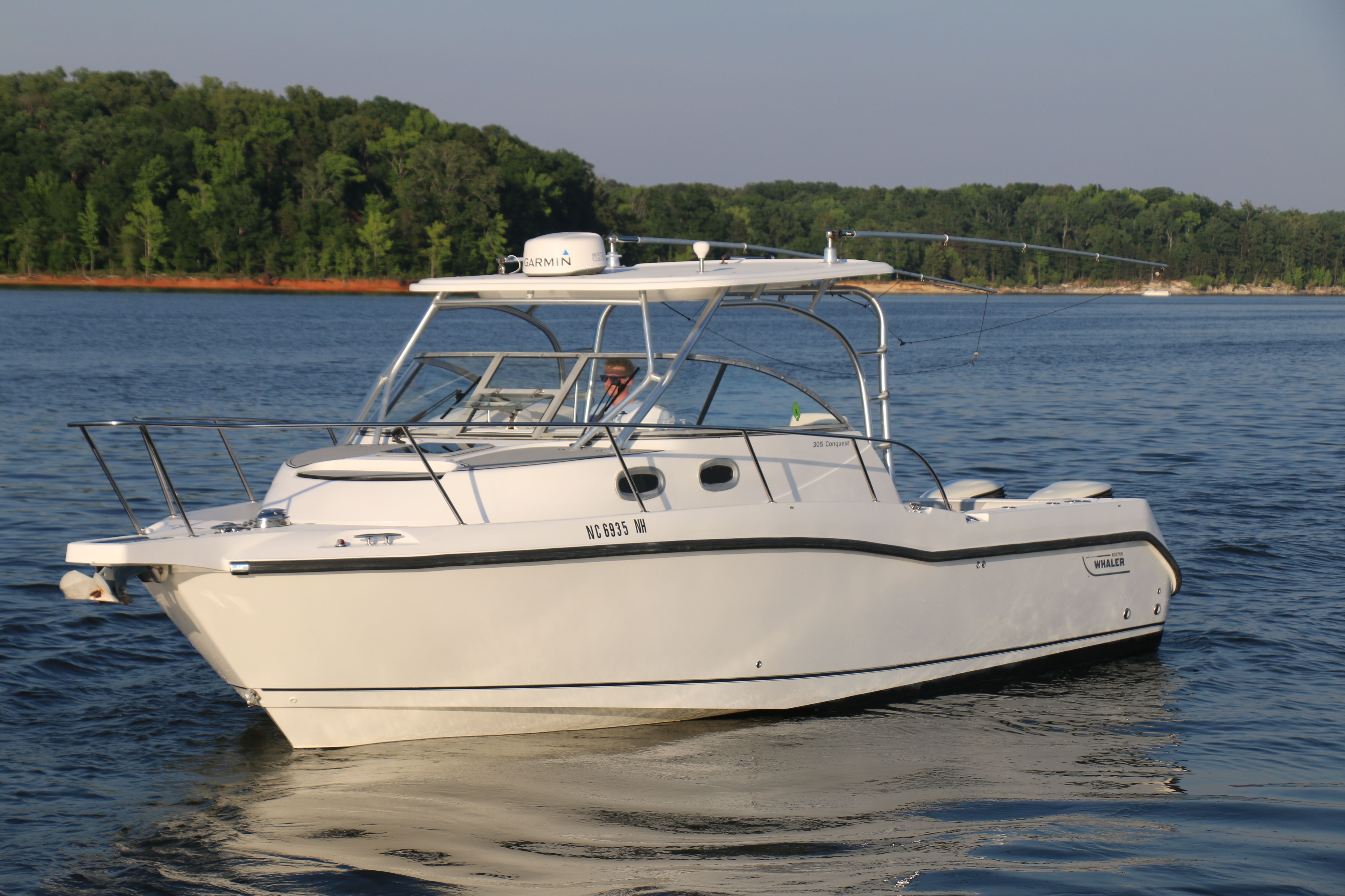A 2006 Boston Whaler 305 Conquest cruising on calm water with a wooded shoreline.