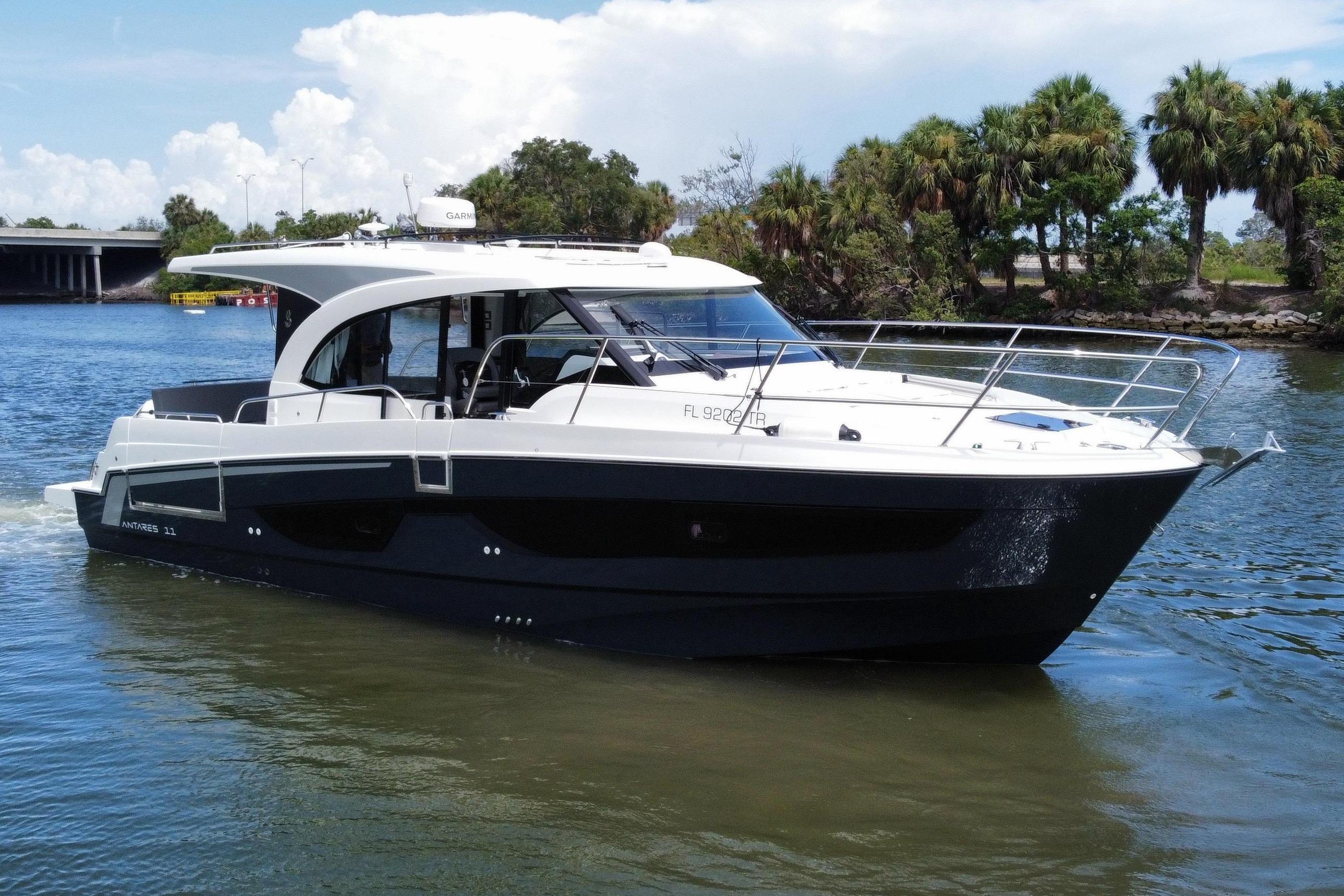 The 2024 Beneteau Antares 11 cruises on a calm river, surrounded by palm trees.