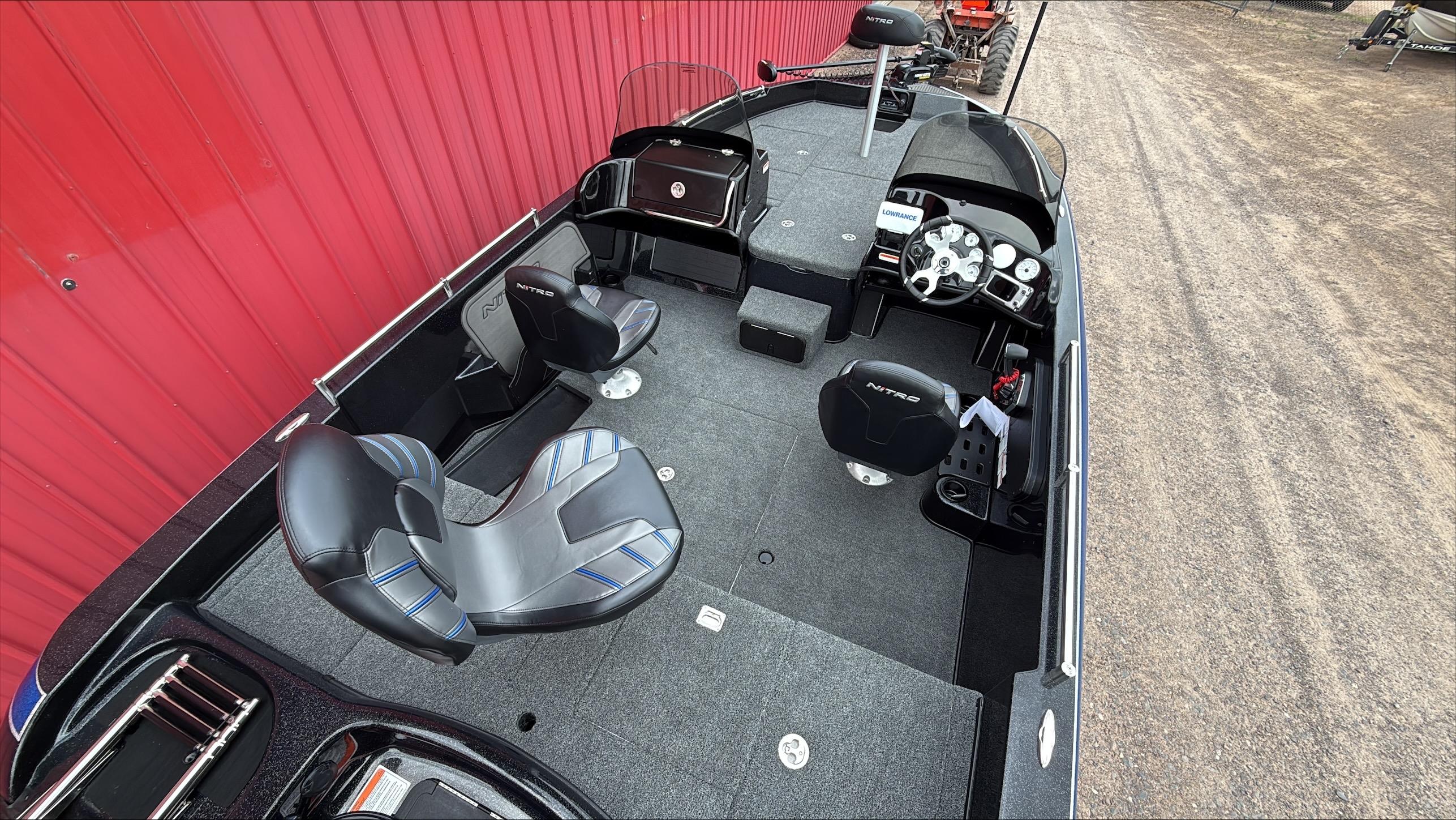 2025 Nitro ZV19 boat interior with modern seating and dashboard, parked beside a red wall.