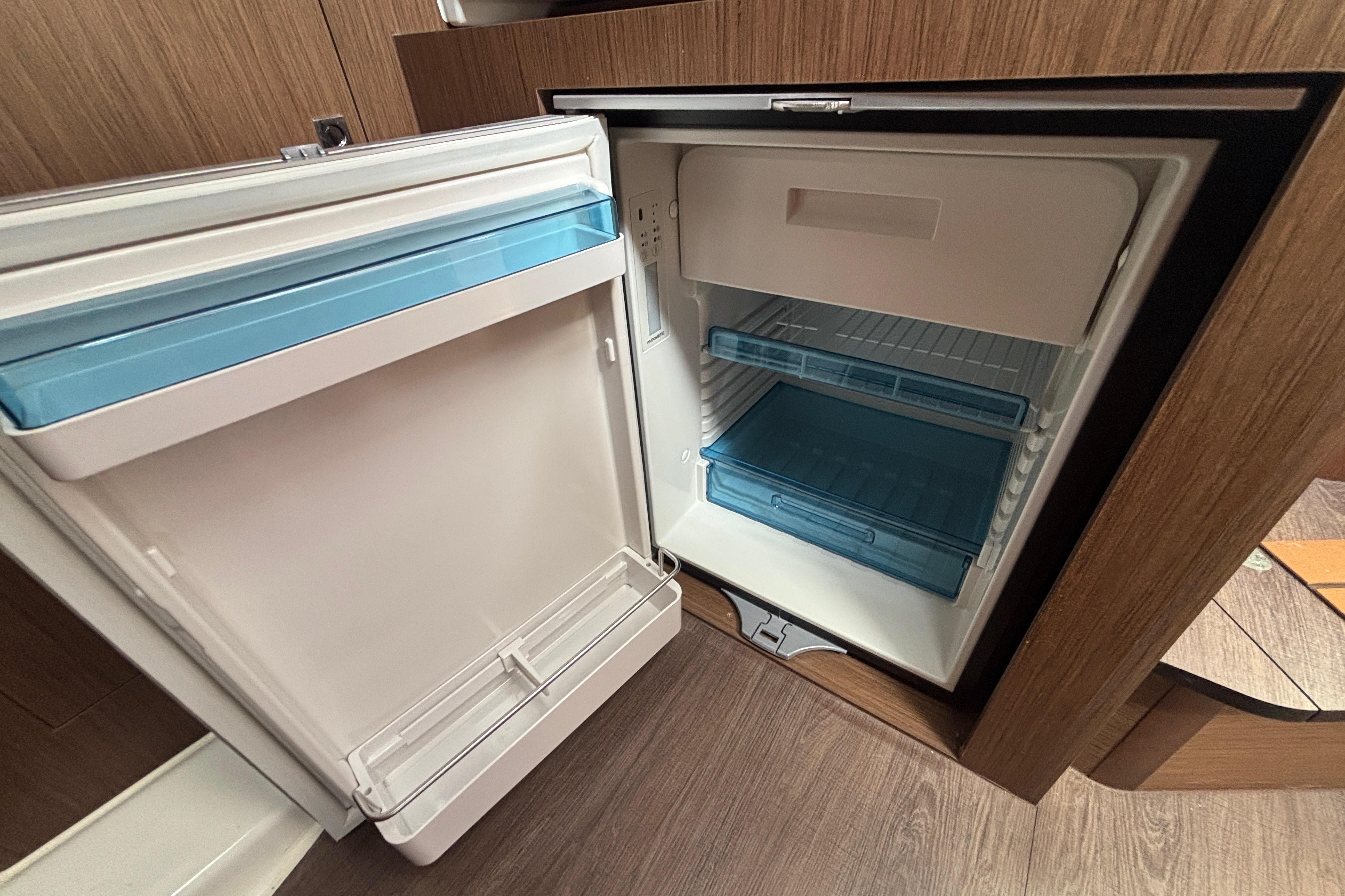 Open refrigerator inside 2024 Beneteau Antares 11 boat, featuring wood paneling and blue shelves.