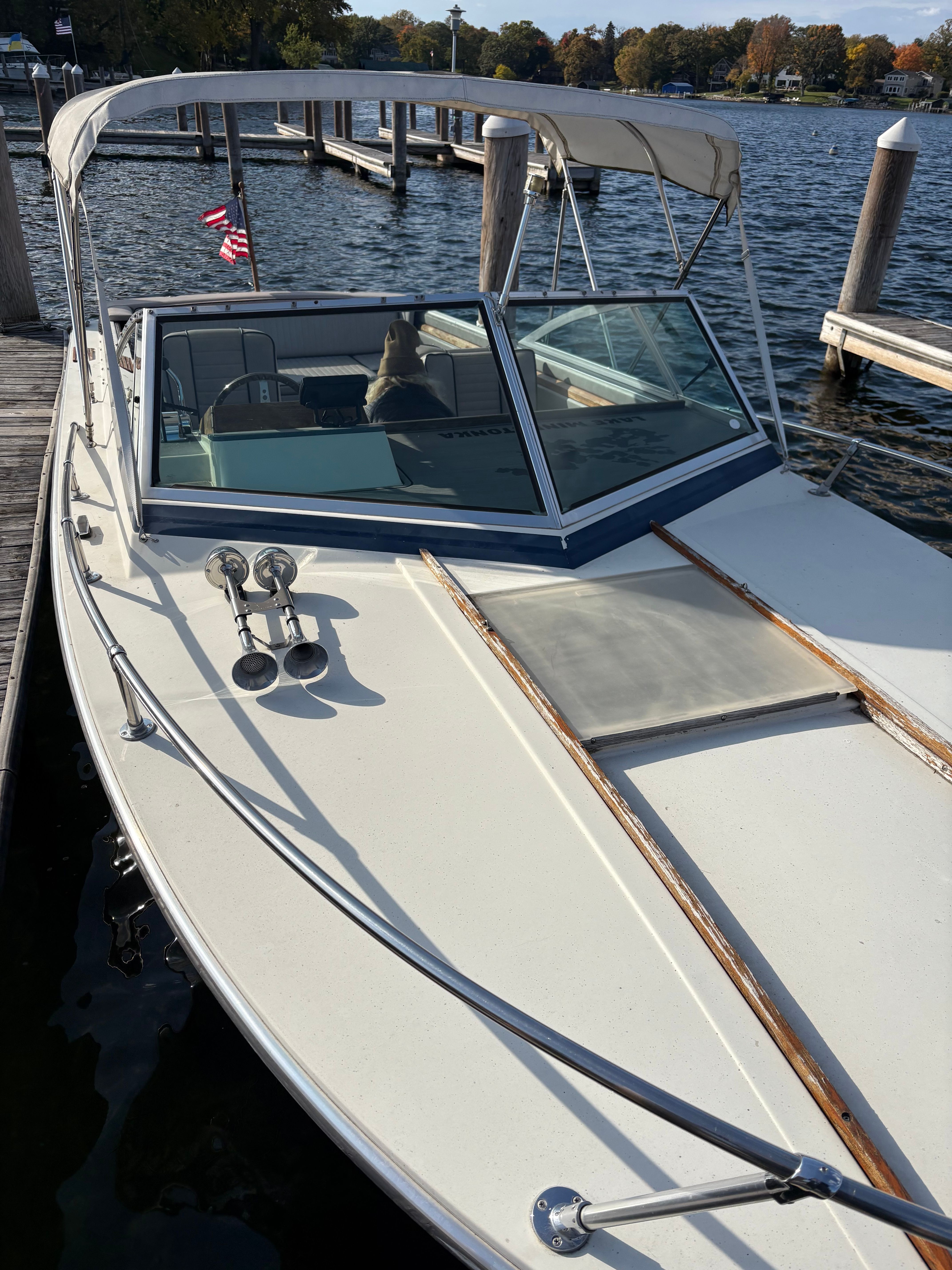 A white motorboat docked, featuring a canopy and American flags, with a calm water backdrop.