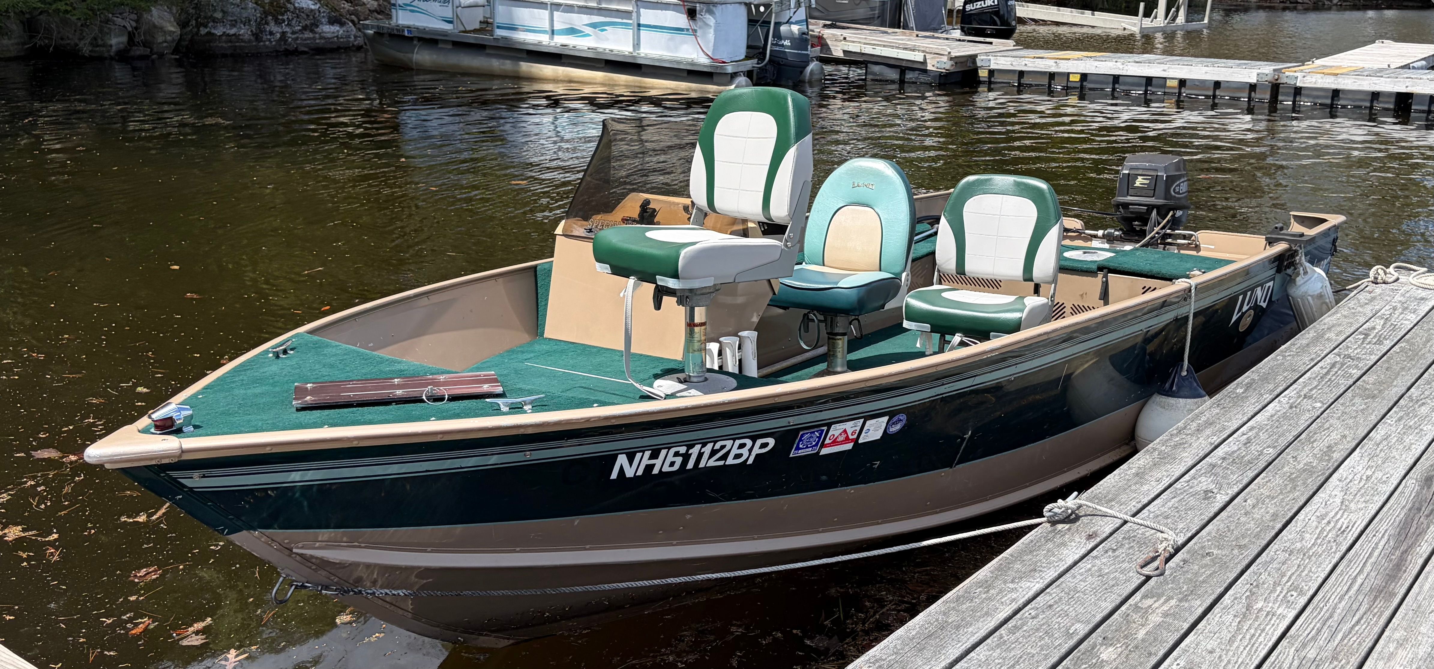 A 1998 Lund Explorer SS docked at a wooden pier. It features green seats and an outboard motor.