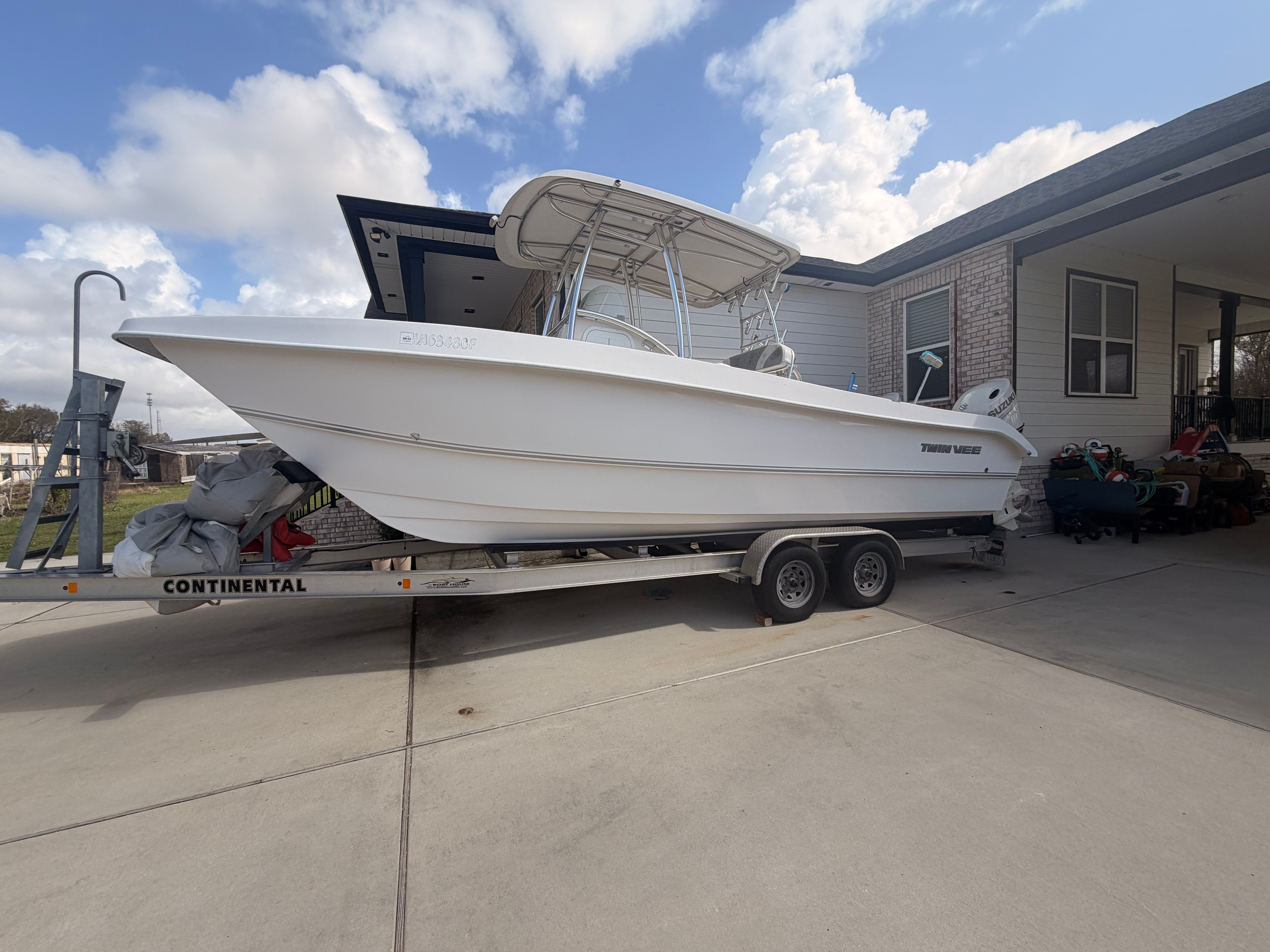 A white Twin Vee Ocean Cat boat is on a trailer in a driveway.