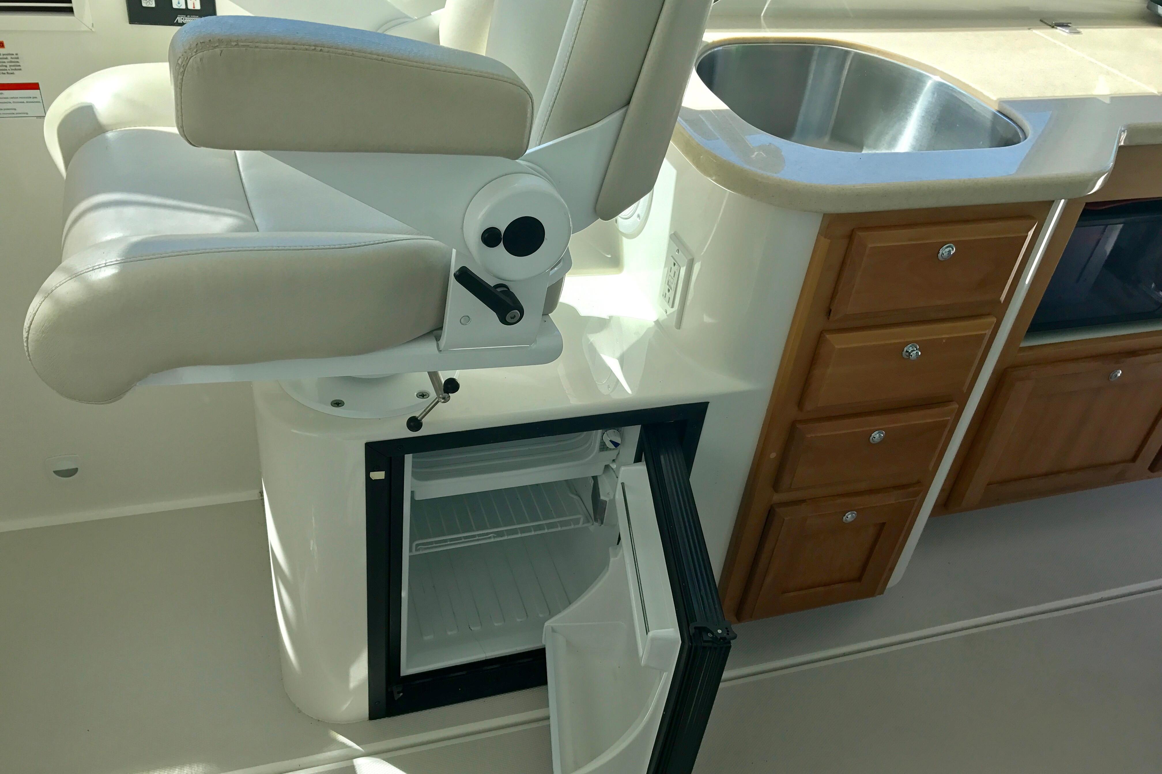 2008 Back Cove 33 interior with helm seat, open fridge, sink, and wooden cabinetry.