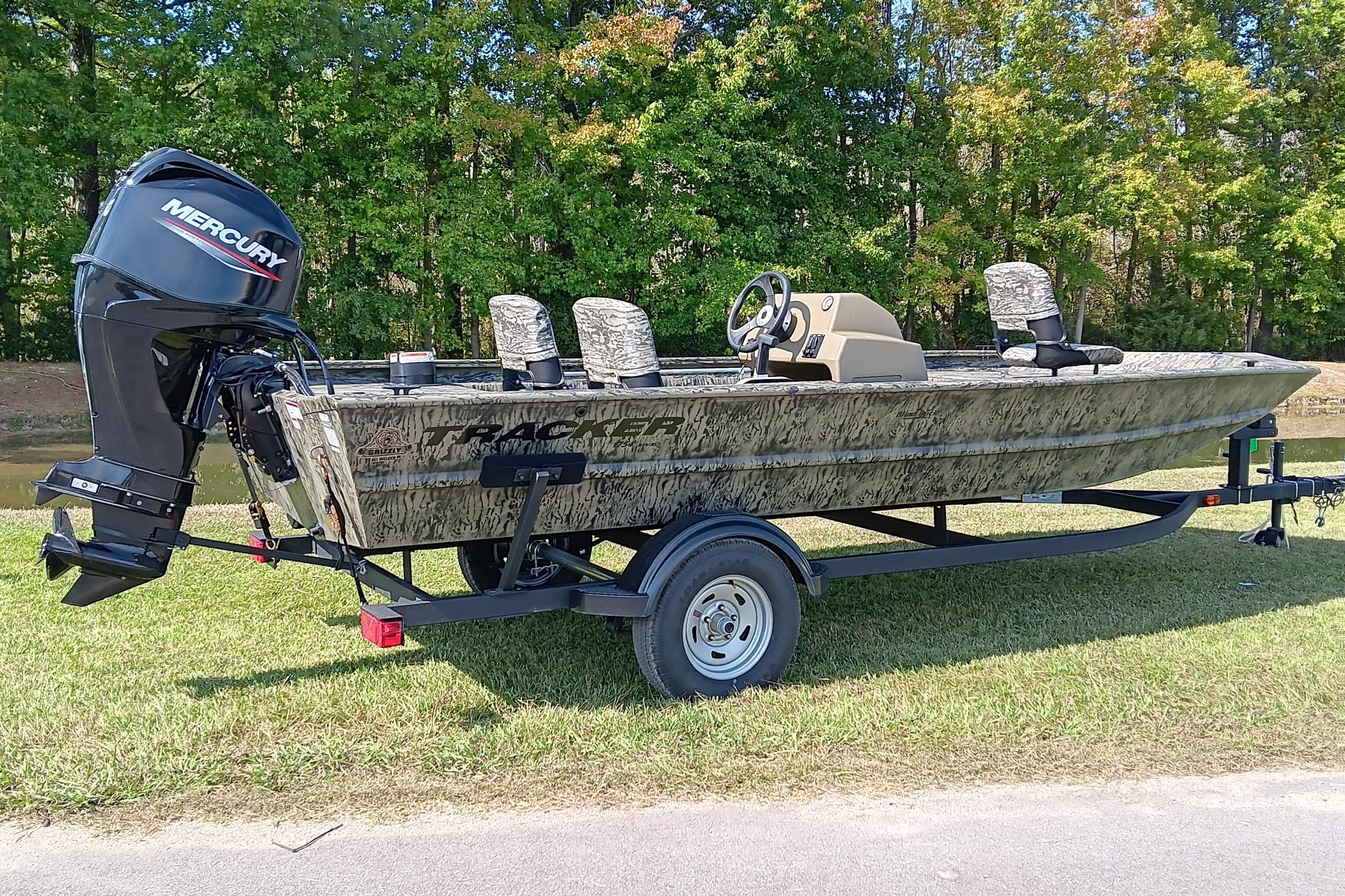 2026 Tracker Grizzly 1754 SC boat with Mercury engine on trailer, parked on grass.