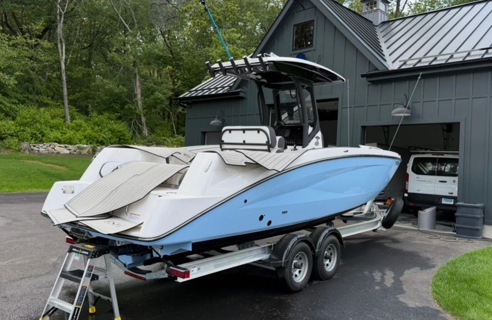 Yamaha 255 FSH Sport H 2024 on a trailer in front of a garage, surrounded by trees.