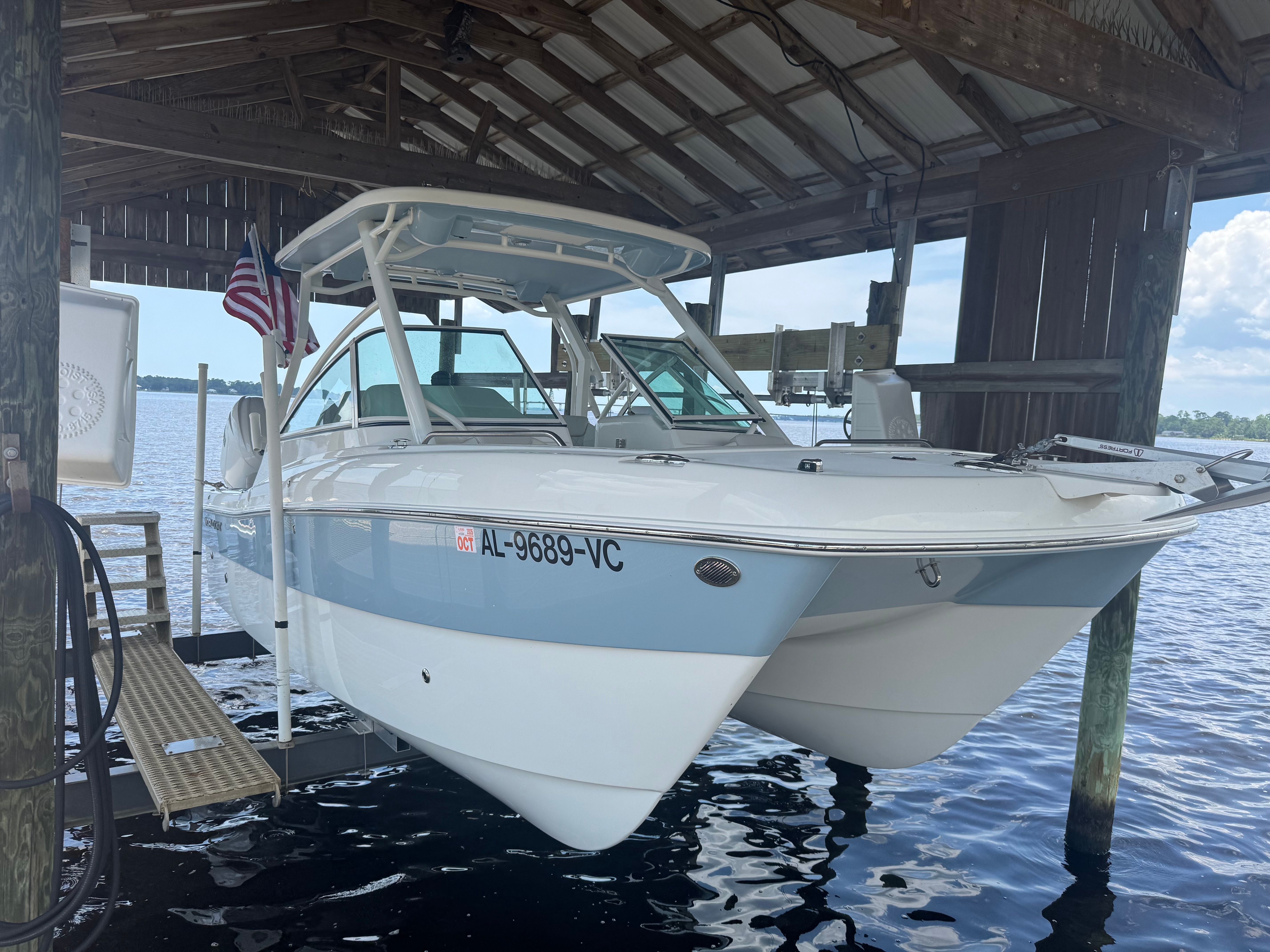 A 2025 World Cat 230 DC is docked in a covered boathouse on the water.