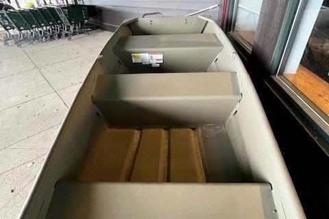 2026 Tracker Grizzly 10 Jon boat, beige interior, displayed outdoors near shopping carts.