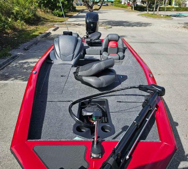 2025 Tracker Pro Team 175 boat with red exterior and gray seating, parked on pavement.