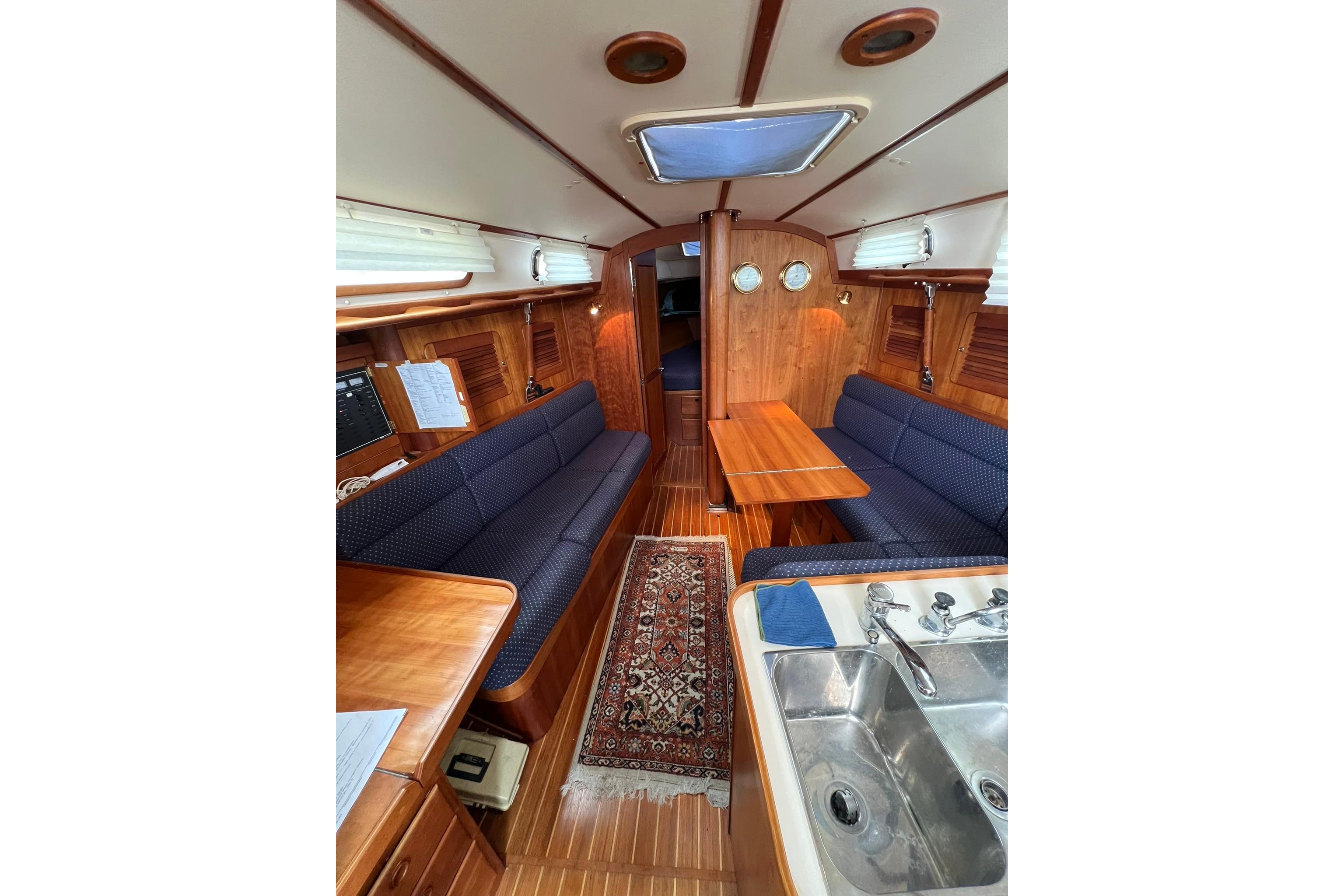 Interior of 1998 Sabre 362 sailboat with wooden finish, blue seating, and compact kitchen area.
