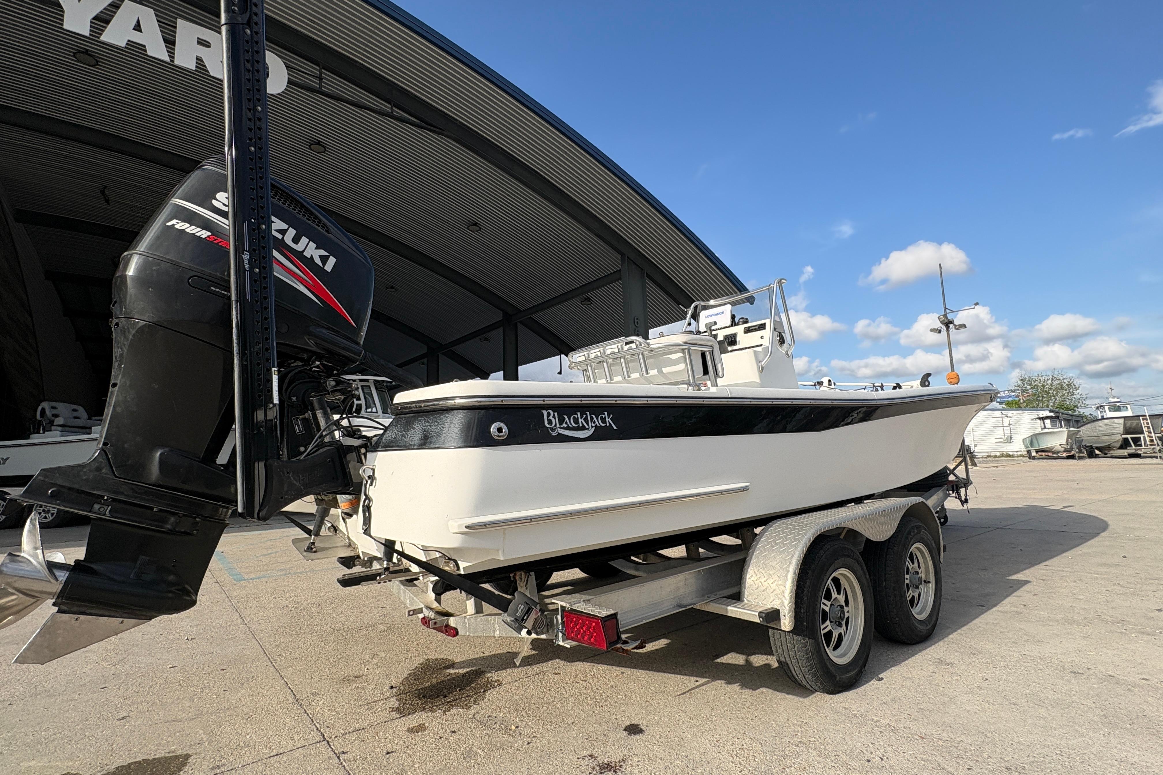 2012 BlackJack 224 boat on trailer with Suzuki outboard motor, parked near a large building.