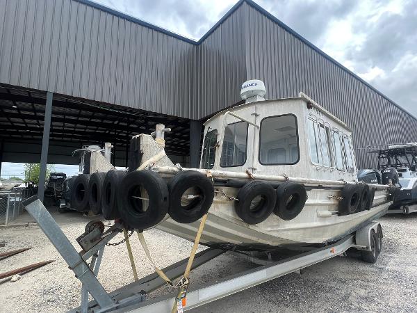 Custom Flat 28 Cabin Boat 2010 on trailer, surrounded by tires, parked near a metal building.