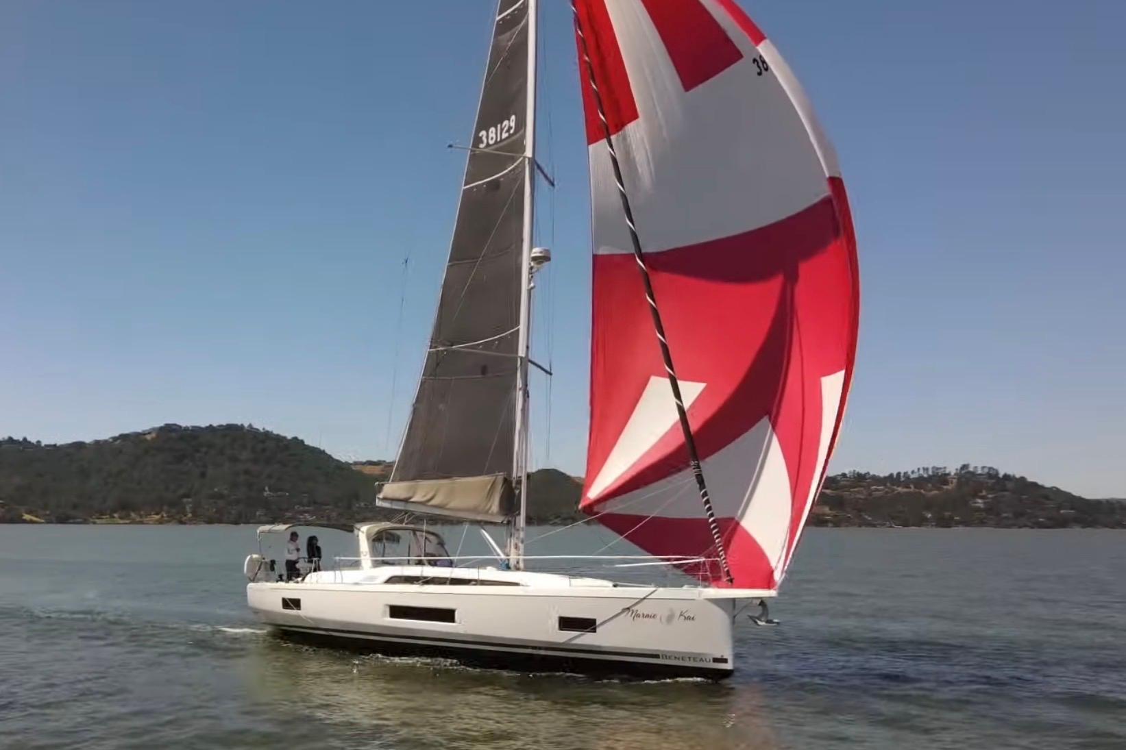 2020 Beneteau Oceanis 46.1 sailing with vibrant red and white spinnaker on a calm lake.