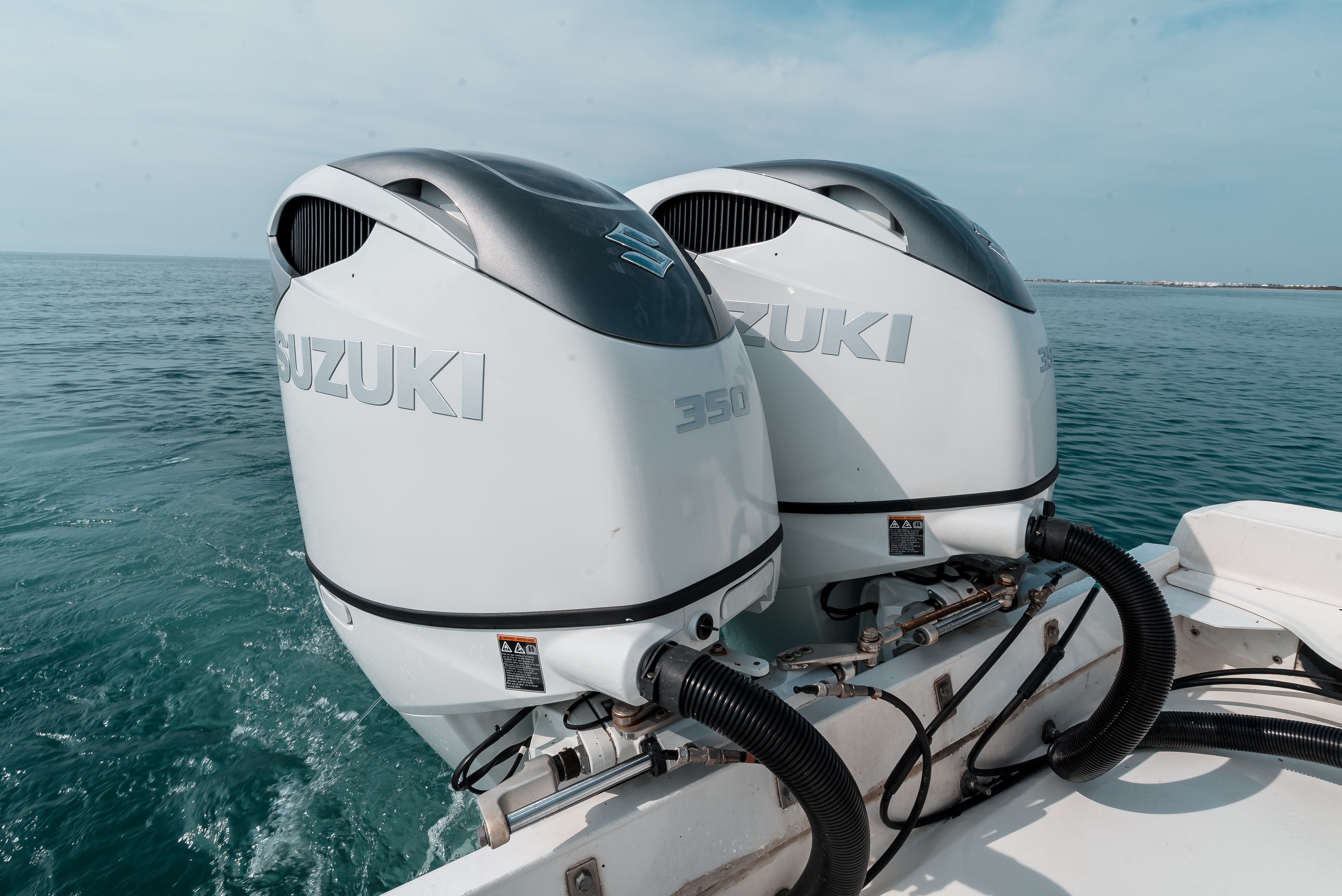 Two Suzuki 350 outboard engines on a boat in calm waters.