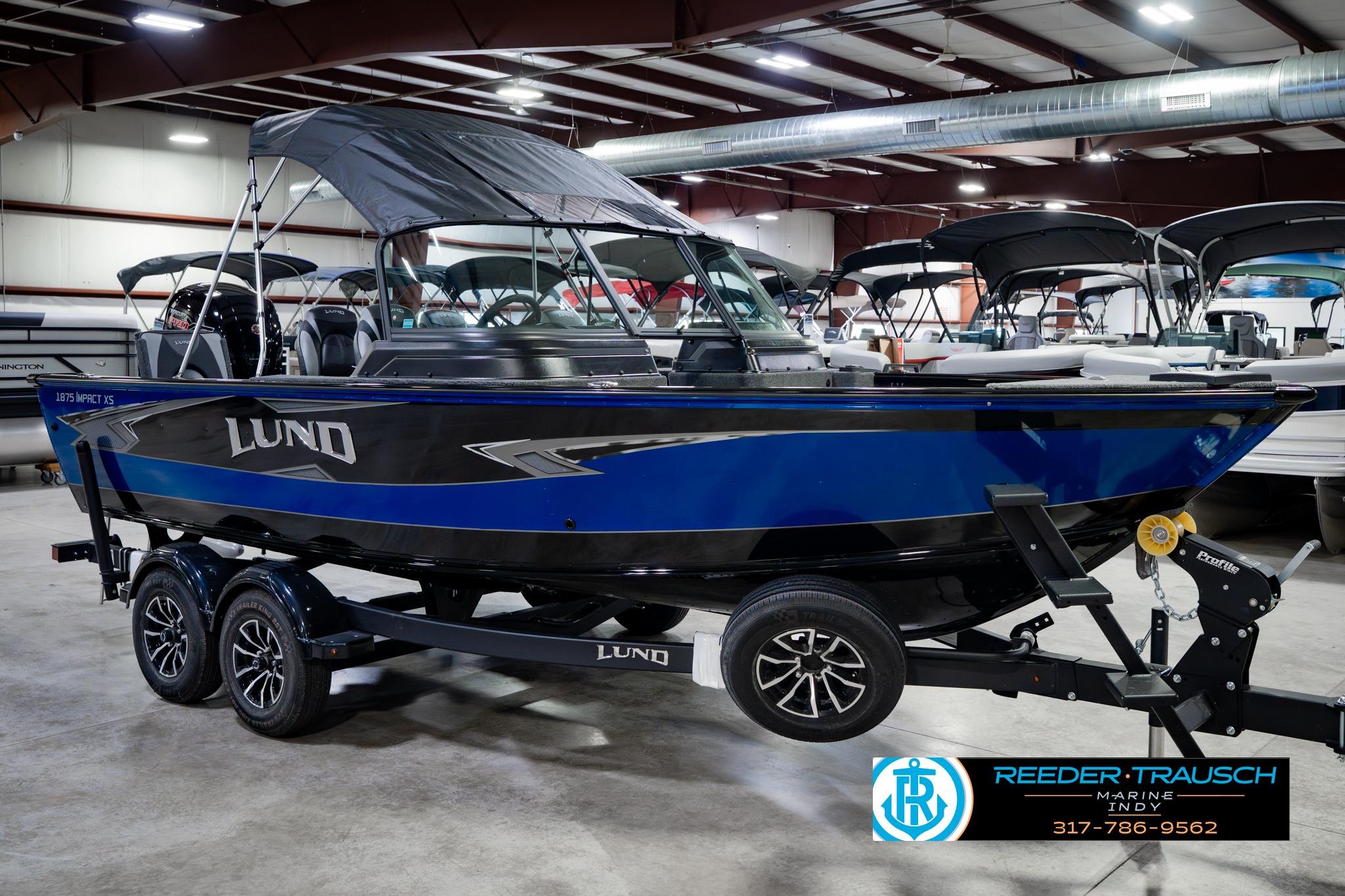 2026 Lund 1875 Impact XS boat in showroom, blue and black design, on trailer.