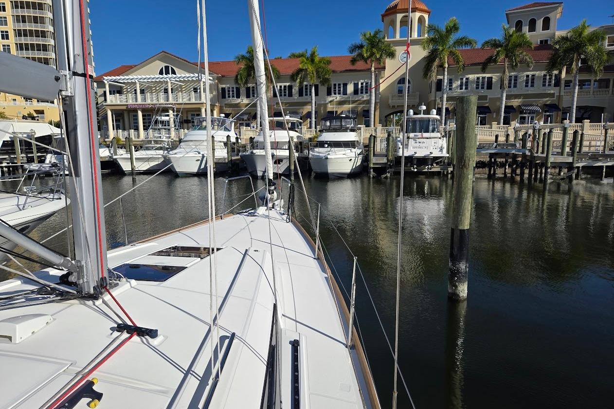 2023 Beneteau Oceanis 38.1 sailboat docked at a marina with palm trees and buildings.