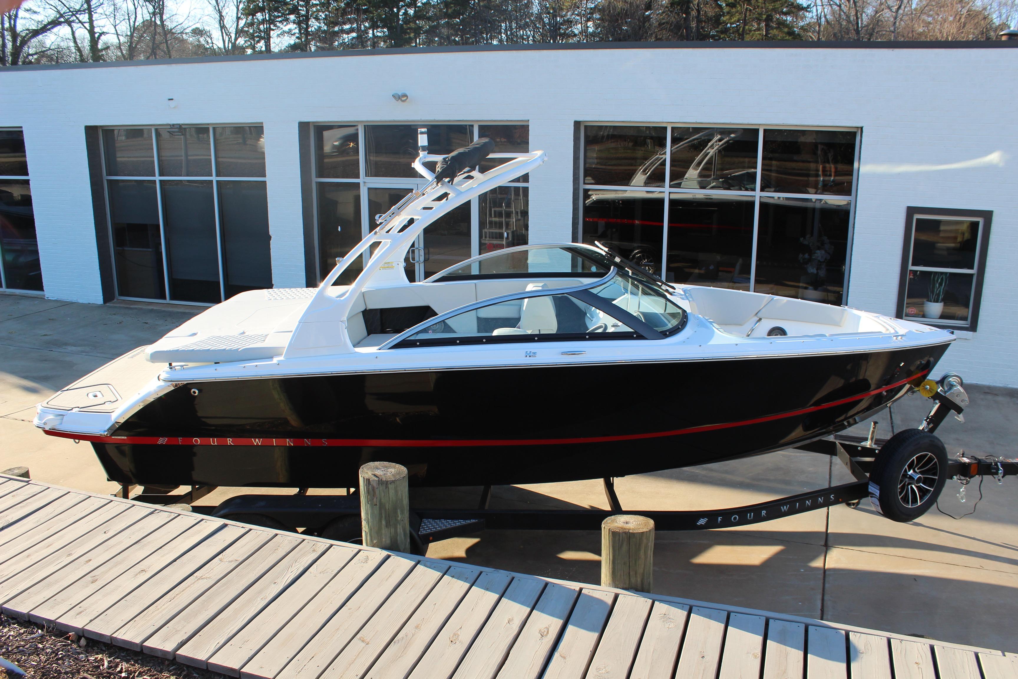 2026 Four Winns H2 Freedom boat on trailer, black with red accents, parked outside.