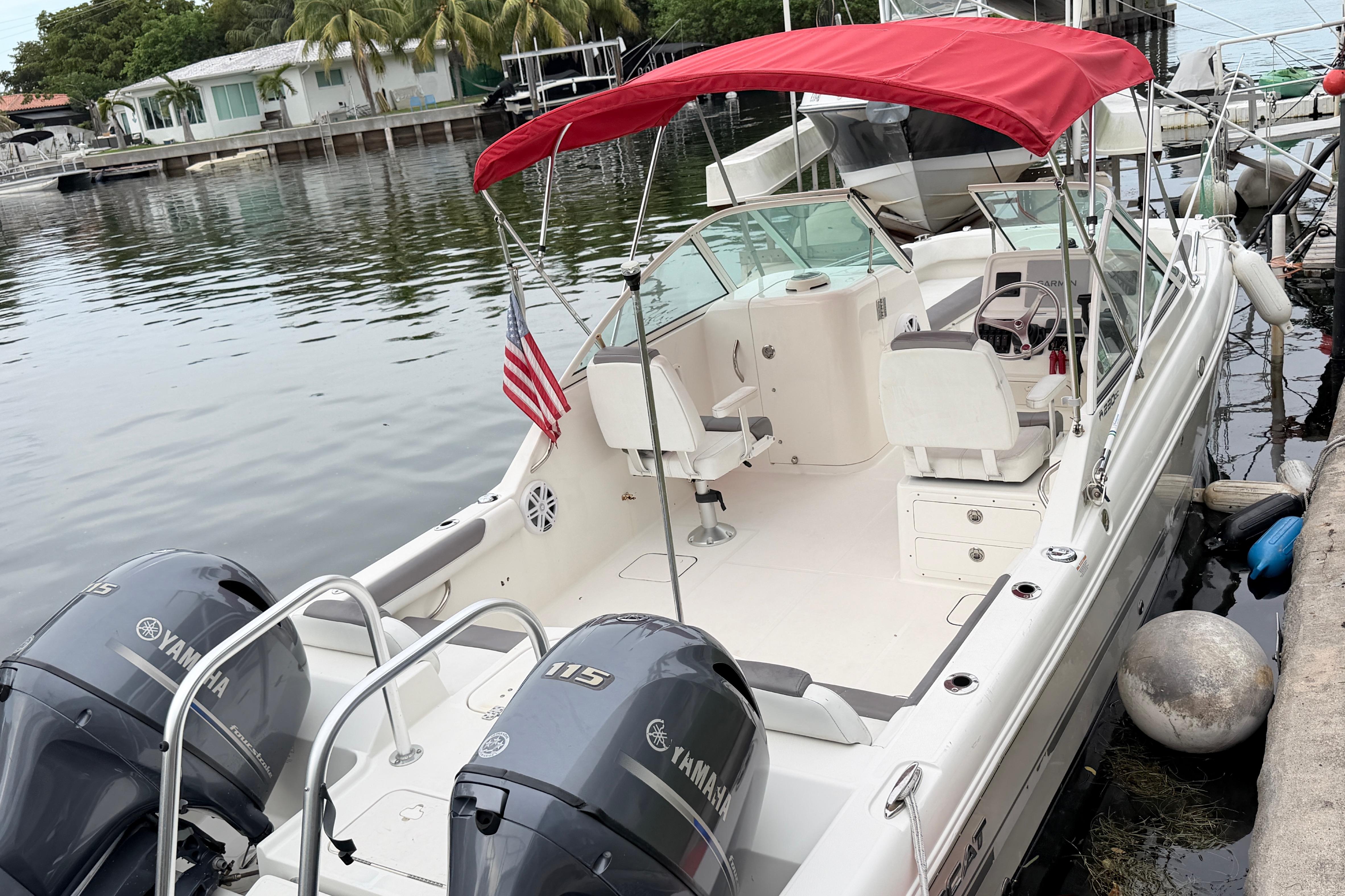 2019 World Cat 230 DC boat with red canopy and twin Yamaha engines docked by the water.