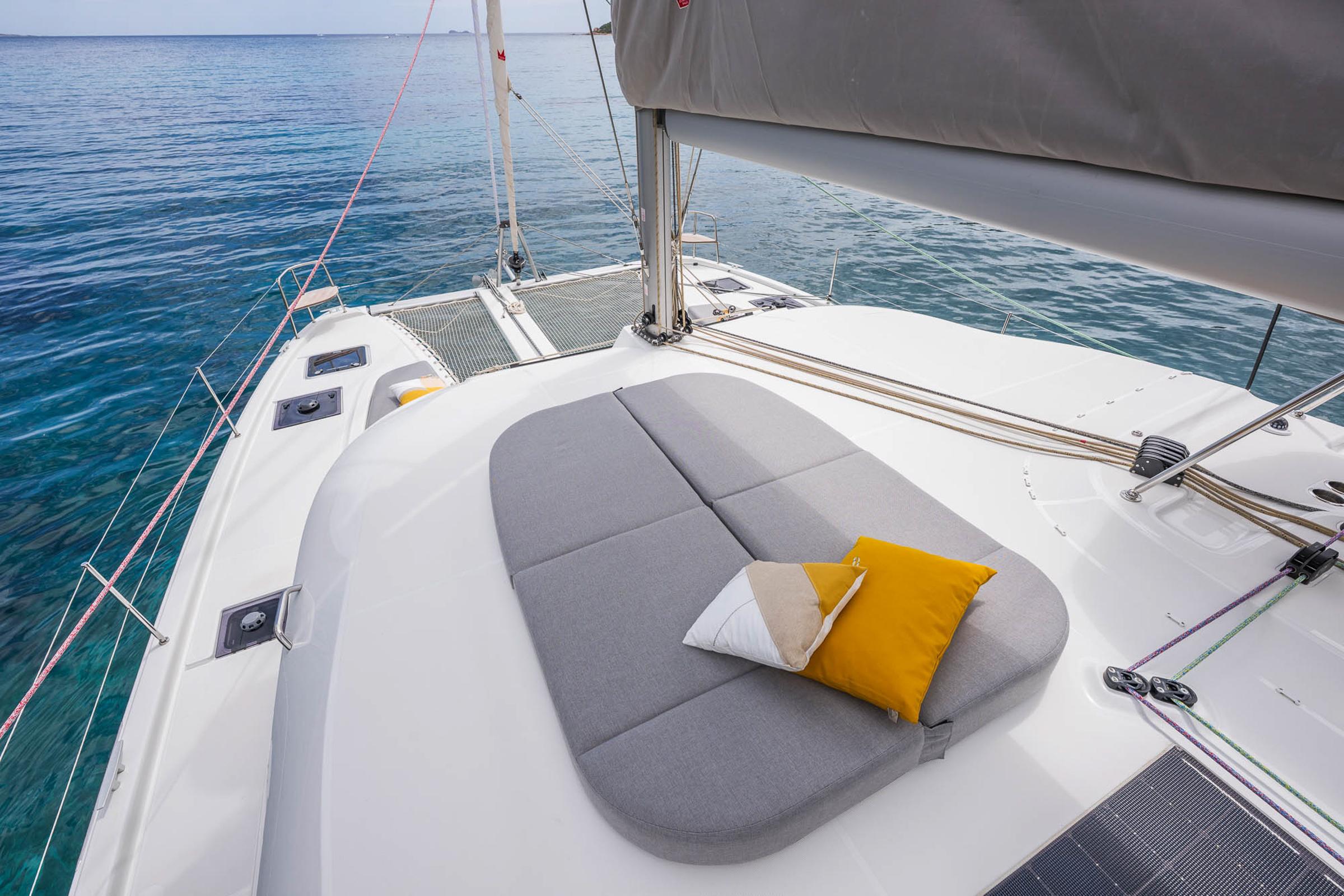 Luxurious 2025 Lagoon 38 catamaran deck with cushions, sailing on clear blue waters.