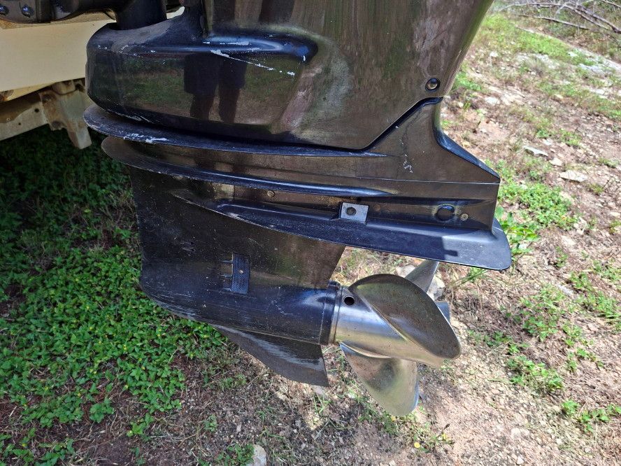 Close-up of an outboard motor with propeller, set on grassy ground.