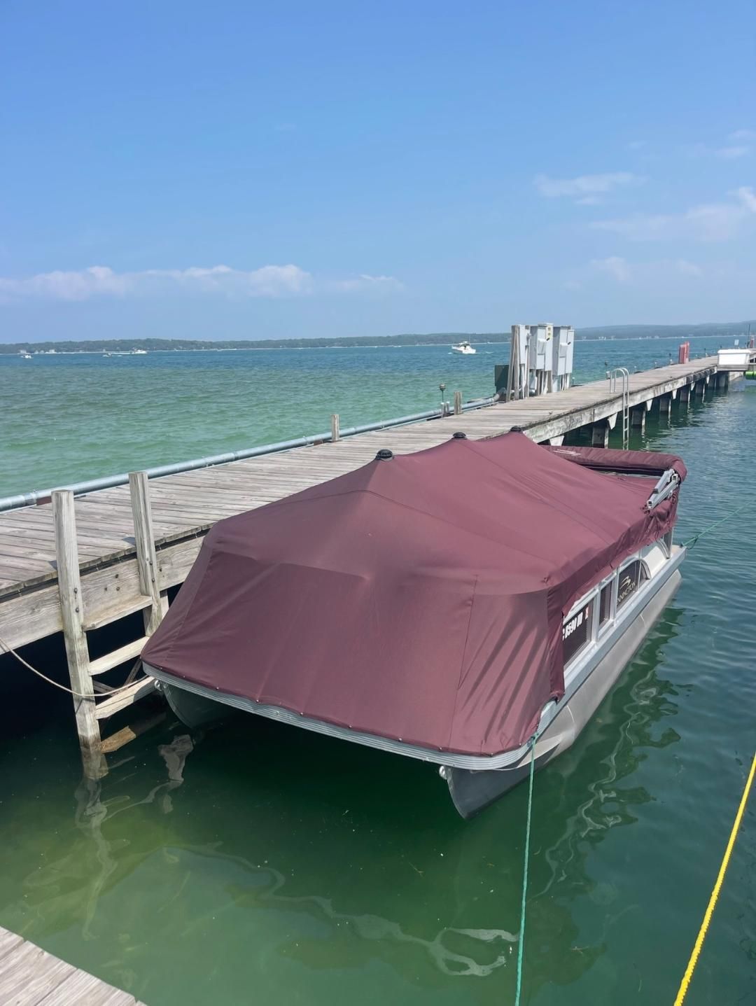 A 2018 Bennington 18SL pontoon boat docked at a wooden pier, covered with a maroon tarp.