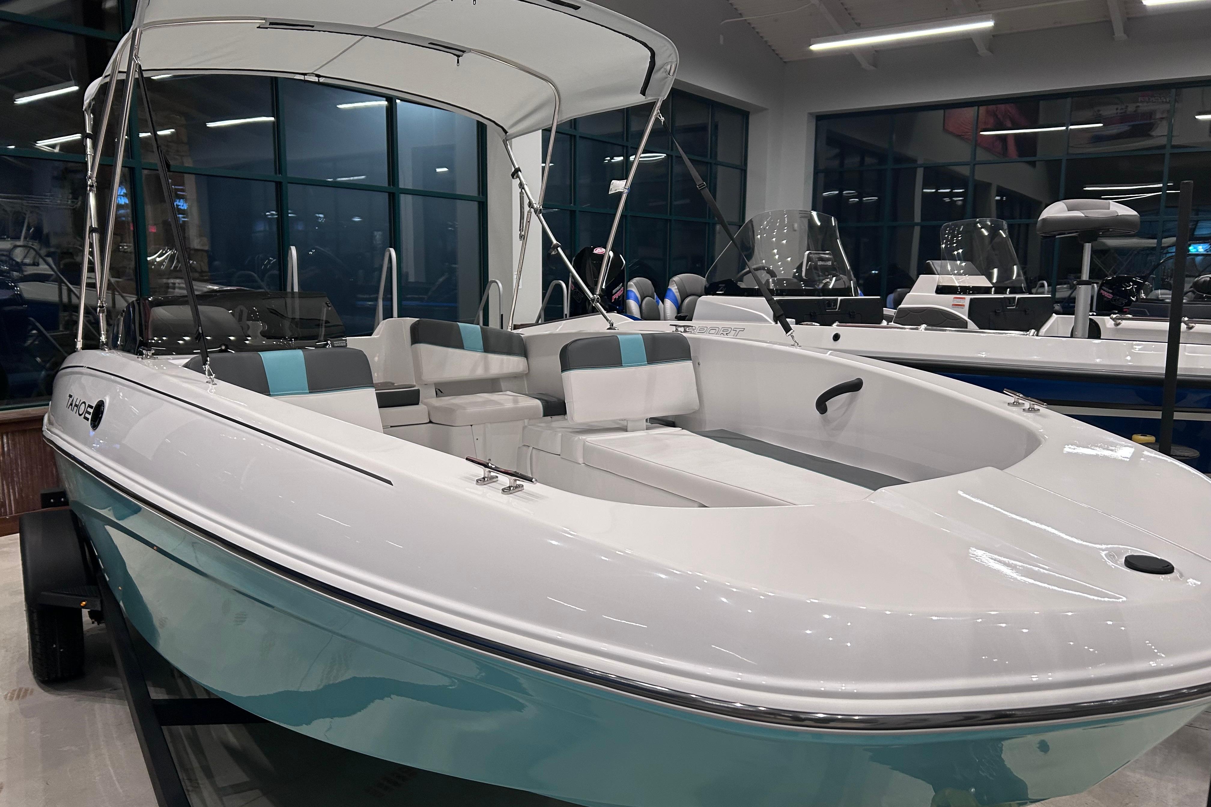 2026 Tahoe T18 boat with canopy, displayed indoors, featuring sleek white and teal design.