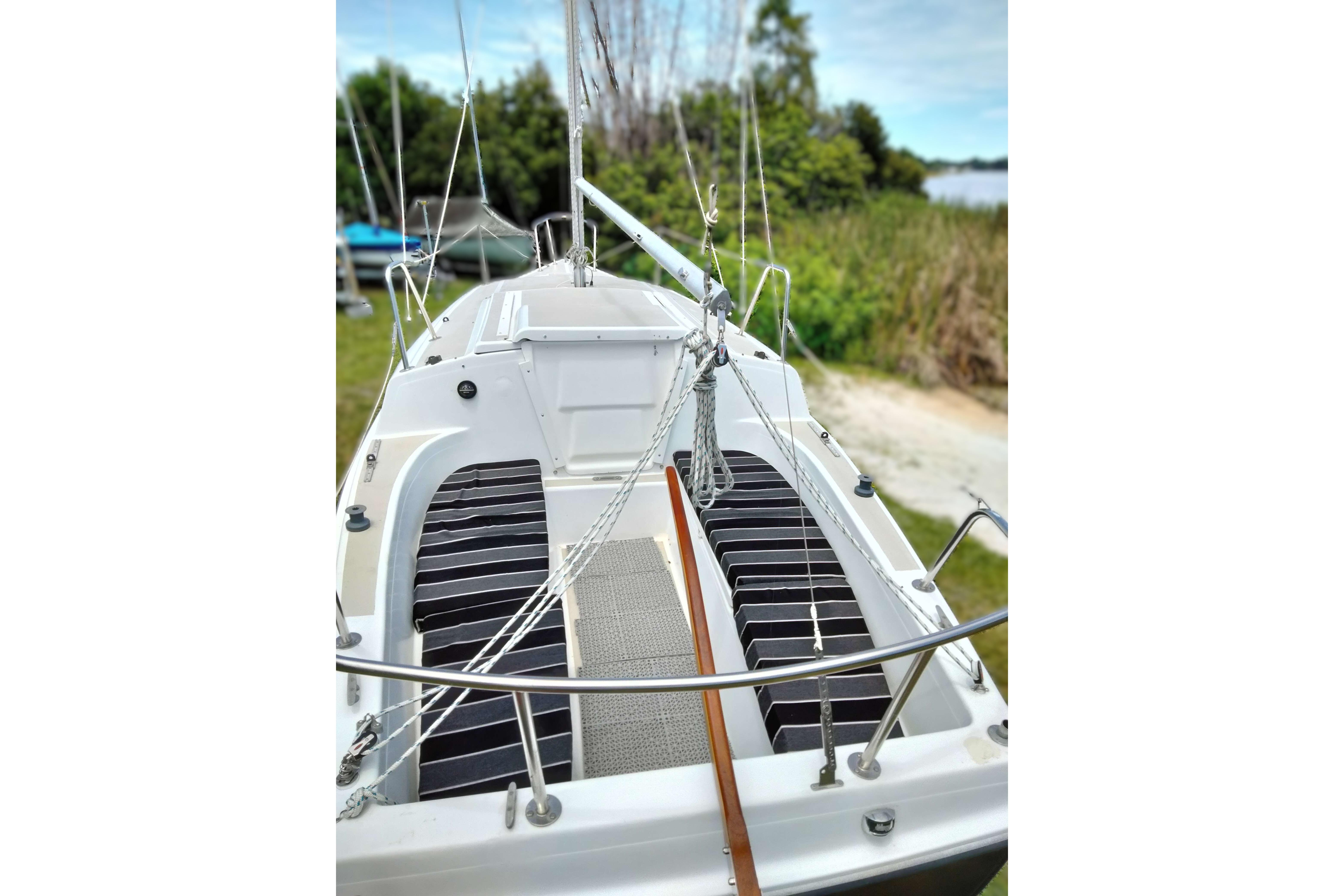1980 MacGregor 25 sailboat deck with rigging, docked near lush greenery.