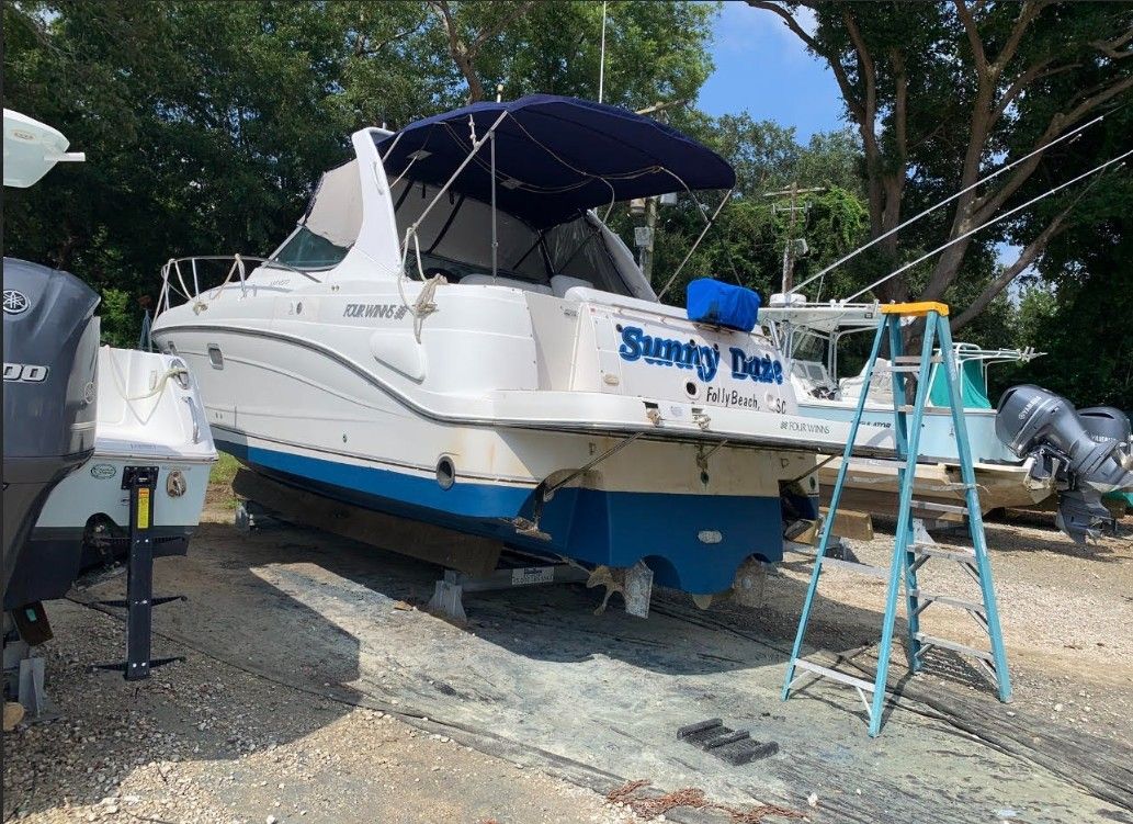 A 2001 Four Winns 338 Vista boat is on dry dock with a blue ladder beside it.