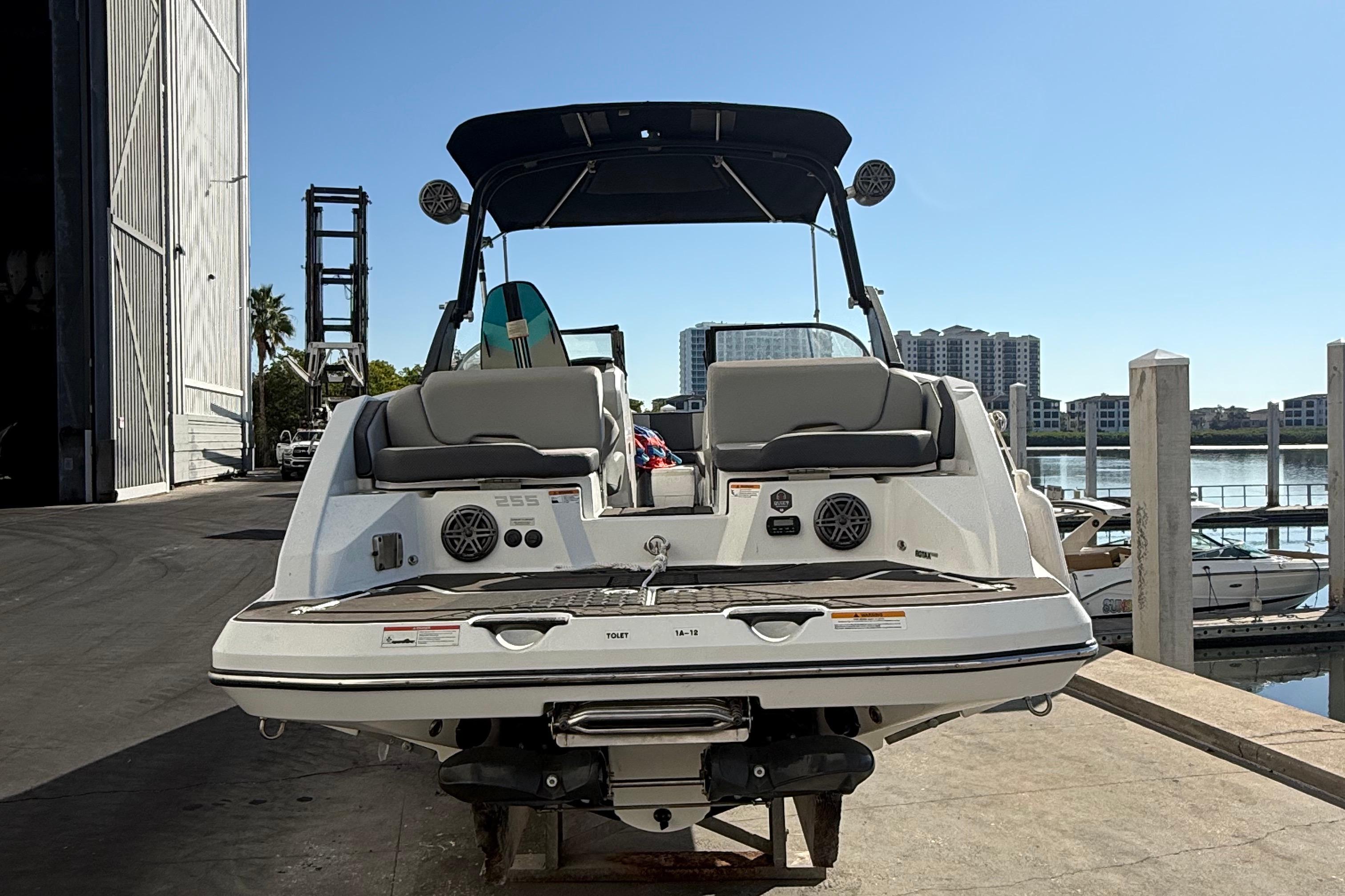 2021 Scarab 255 ID boat docked, rear view with seating and speakers, sunny marina backdrop.