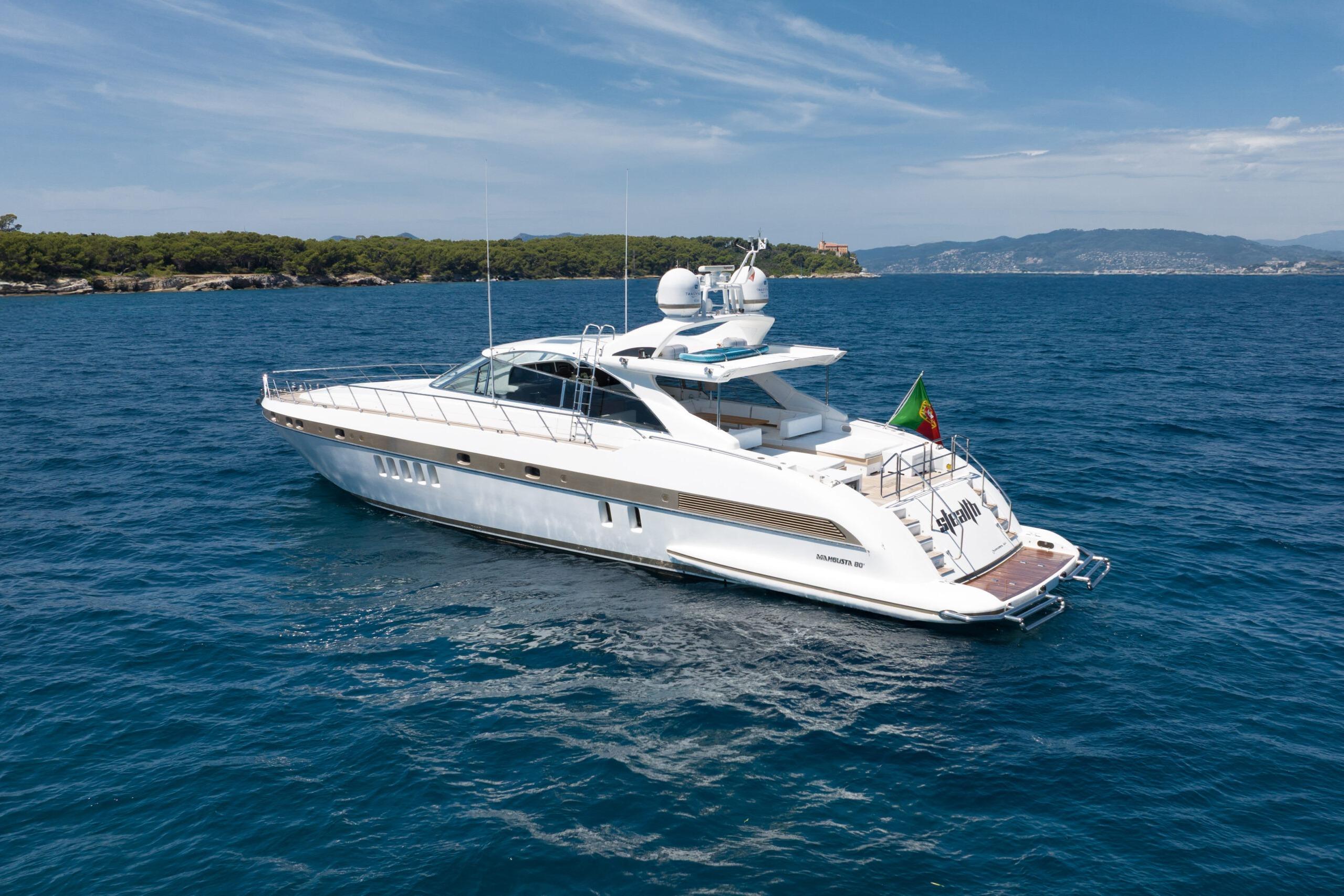 2006 Mangusta 80 yacht cruising on blue ocean near scenic coastline.