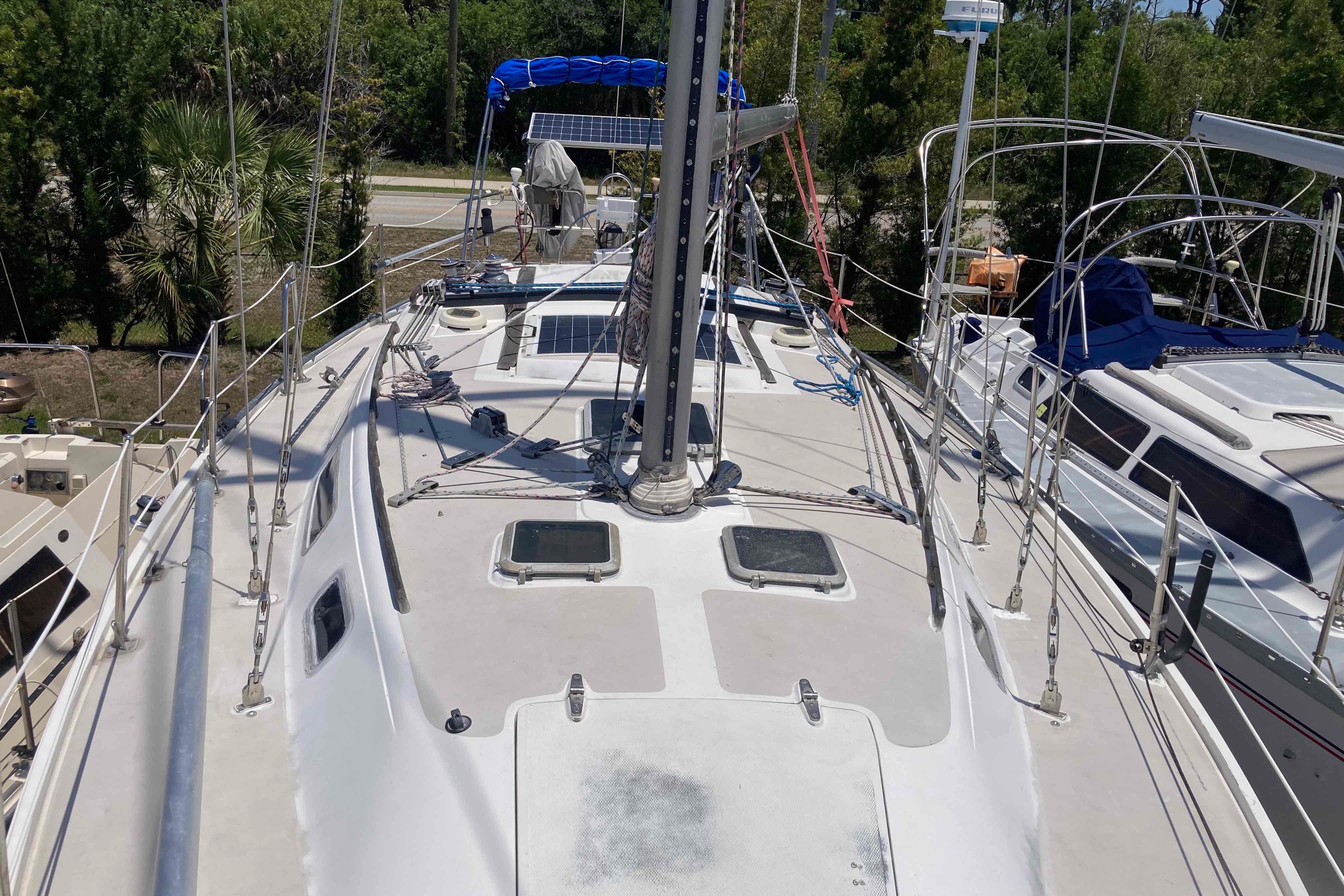 1984 Catalina 36 sailboat deck with rigging and solar panels, docked near trees.