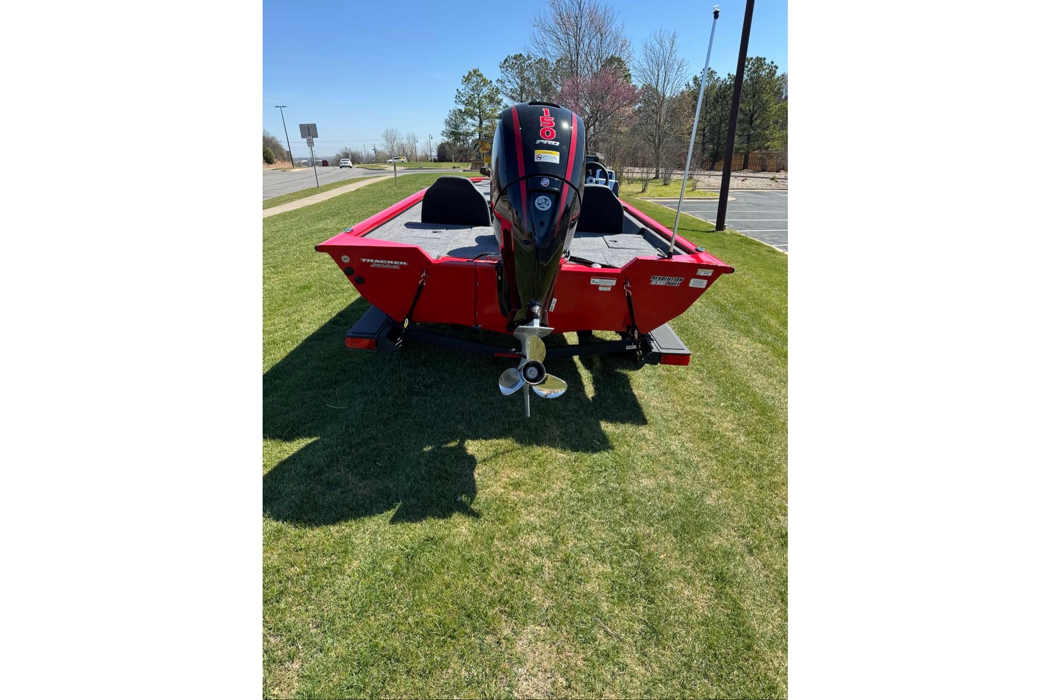 Red 2026 Tracker Pro Team 195 boat with outboard motor on grass.