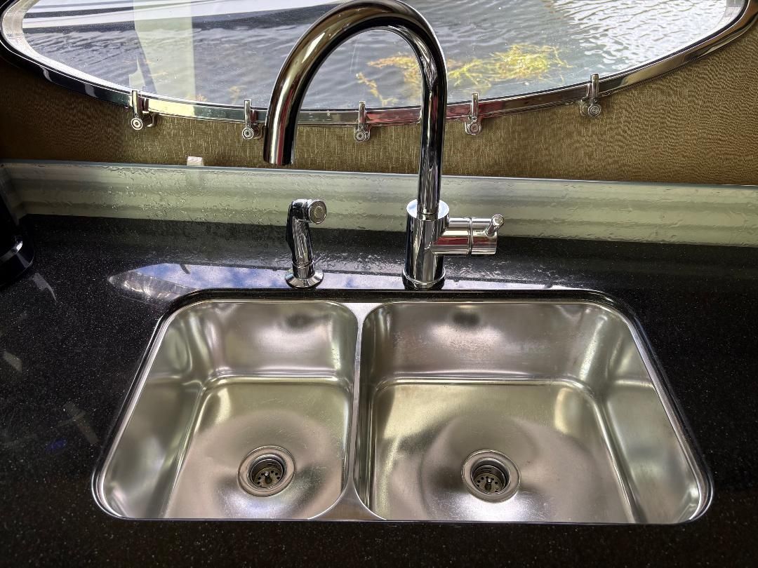 Double stainless steel sink with modern faucet, set in a dark countertop, in front of a boat window.