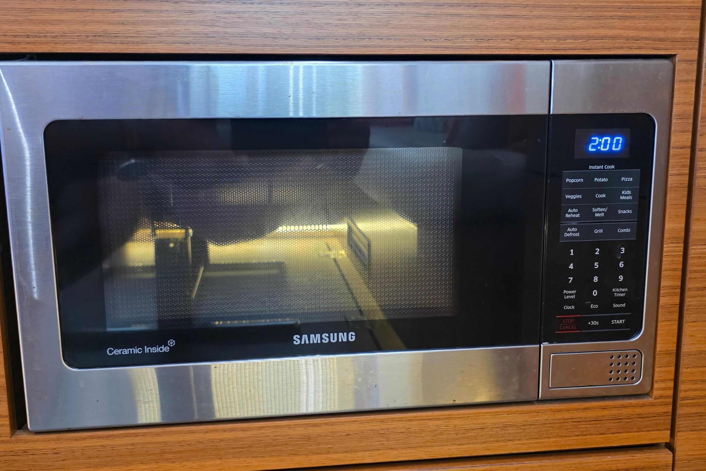 Modern Samsung microwave with digital display, set in a wooden kitchen cabinet.