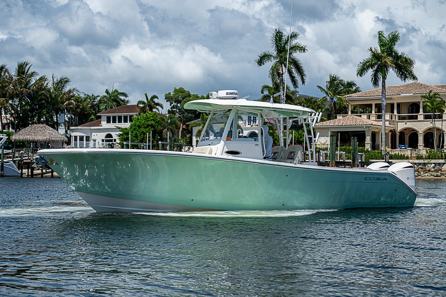 2019 Cobia 320 Center Console boat cruising near luxury waterfront homes and palm trees.