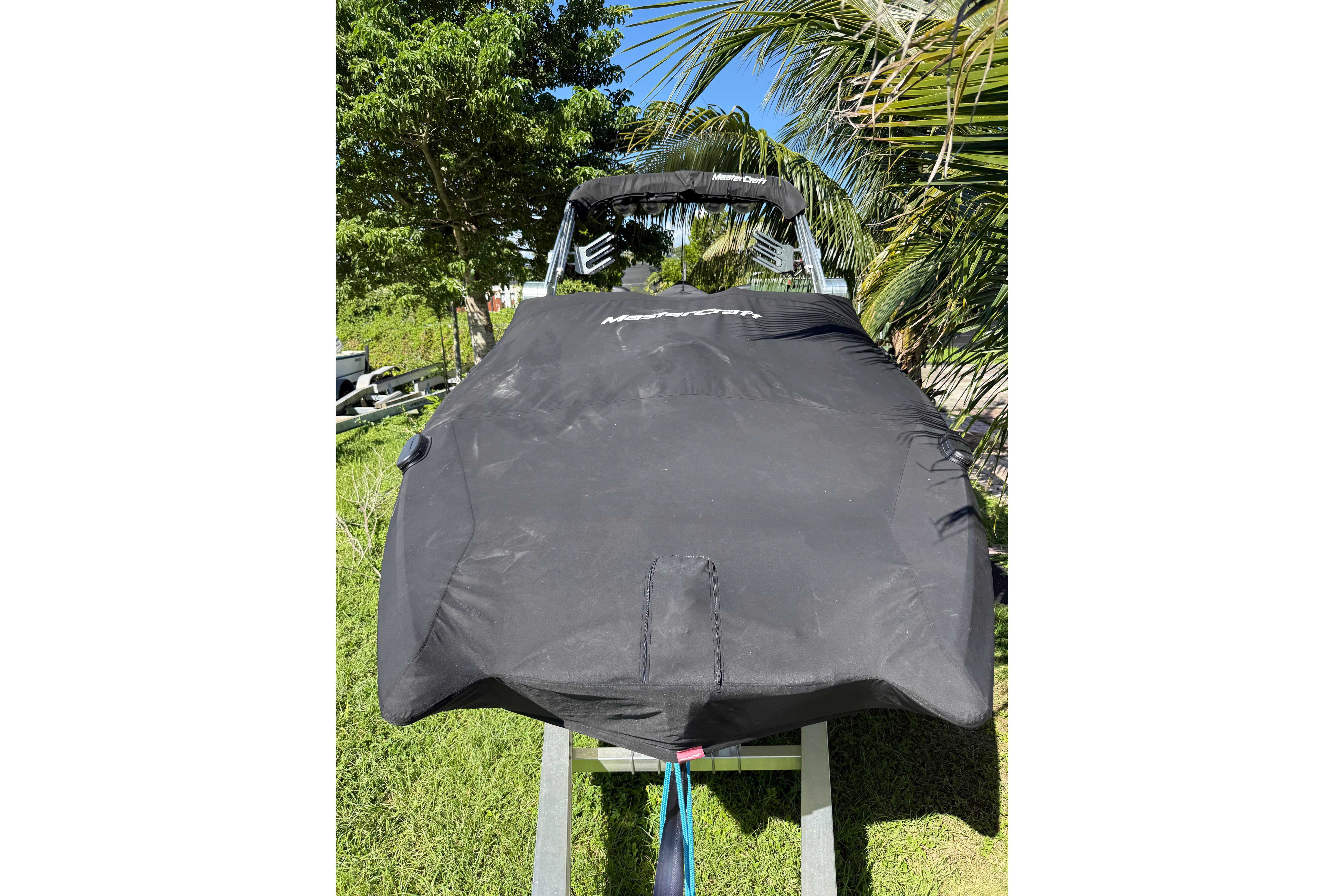 2023 MasterCraft X24 boat covered, surrounded by lush greenery.