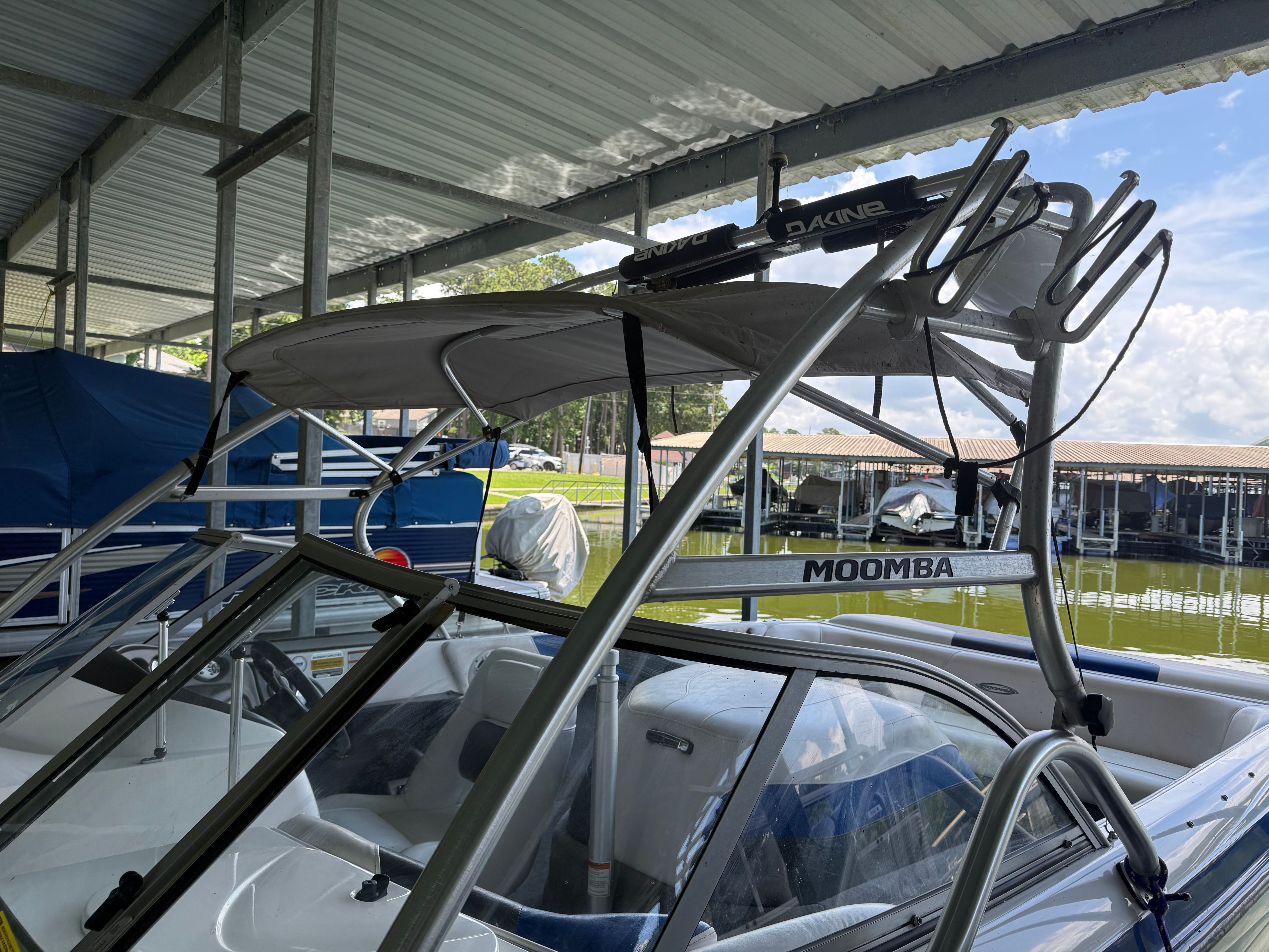 A 2005 Moomba Mobius LS boat under a covered dock with wakeboard racks.