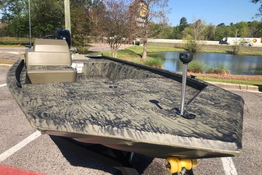 2026 Tracker Grizzly 1648 SC boat parked near a pond, showcasing its camouflage design.