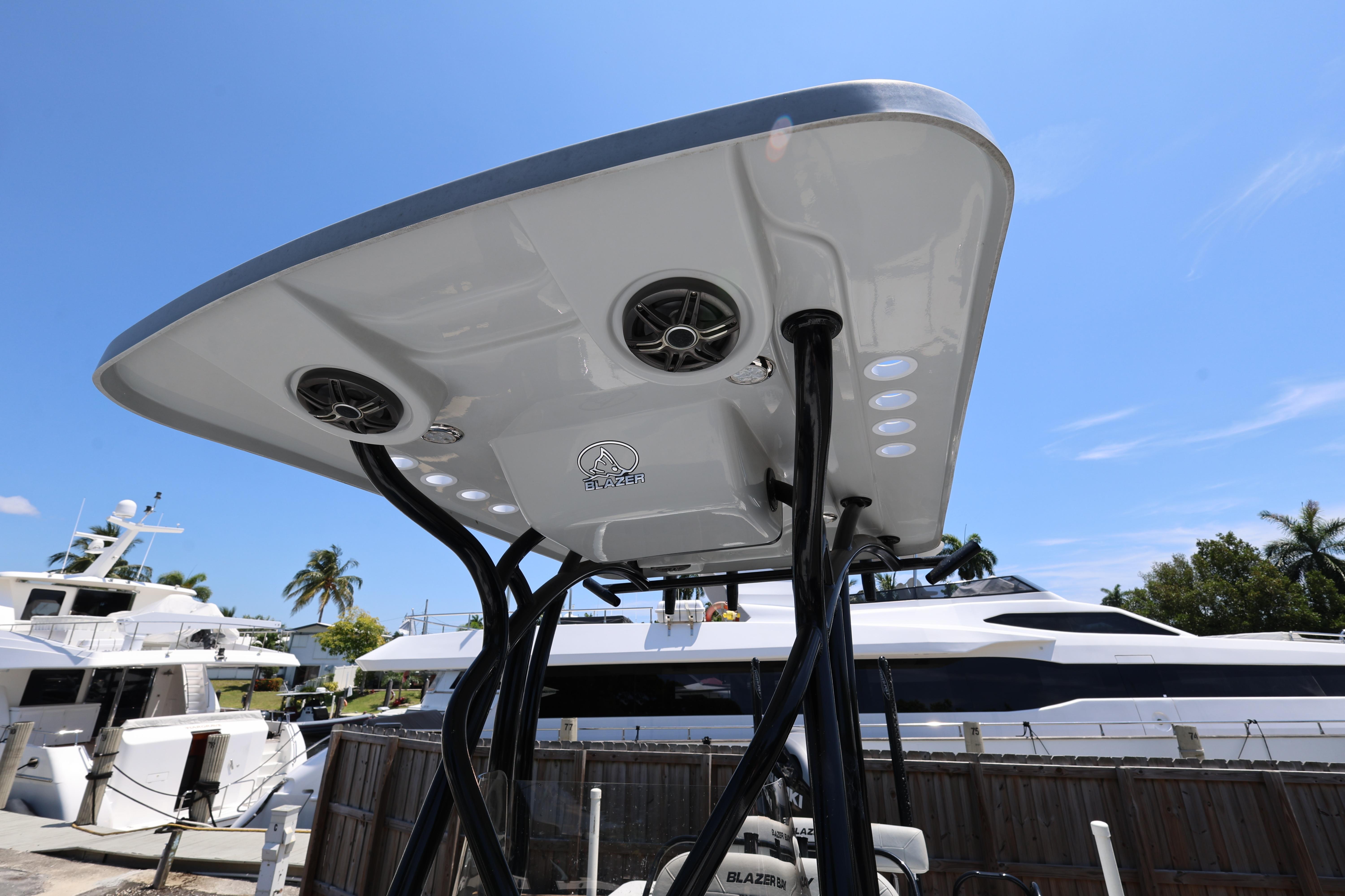 2021 Blazer Bay 2400 boat with T-top speakers and lights, docked near yachts.