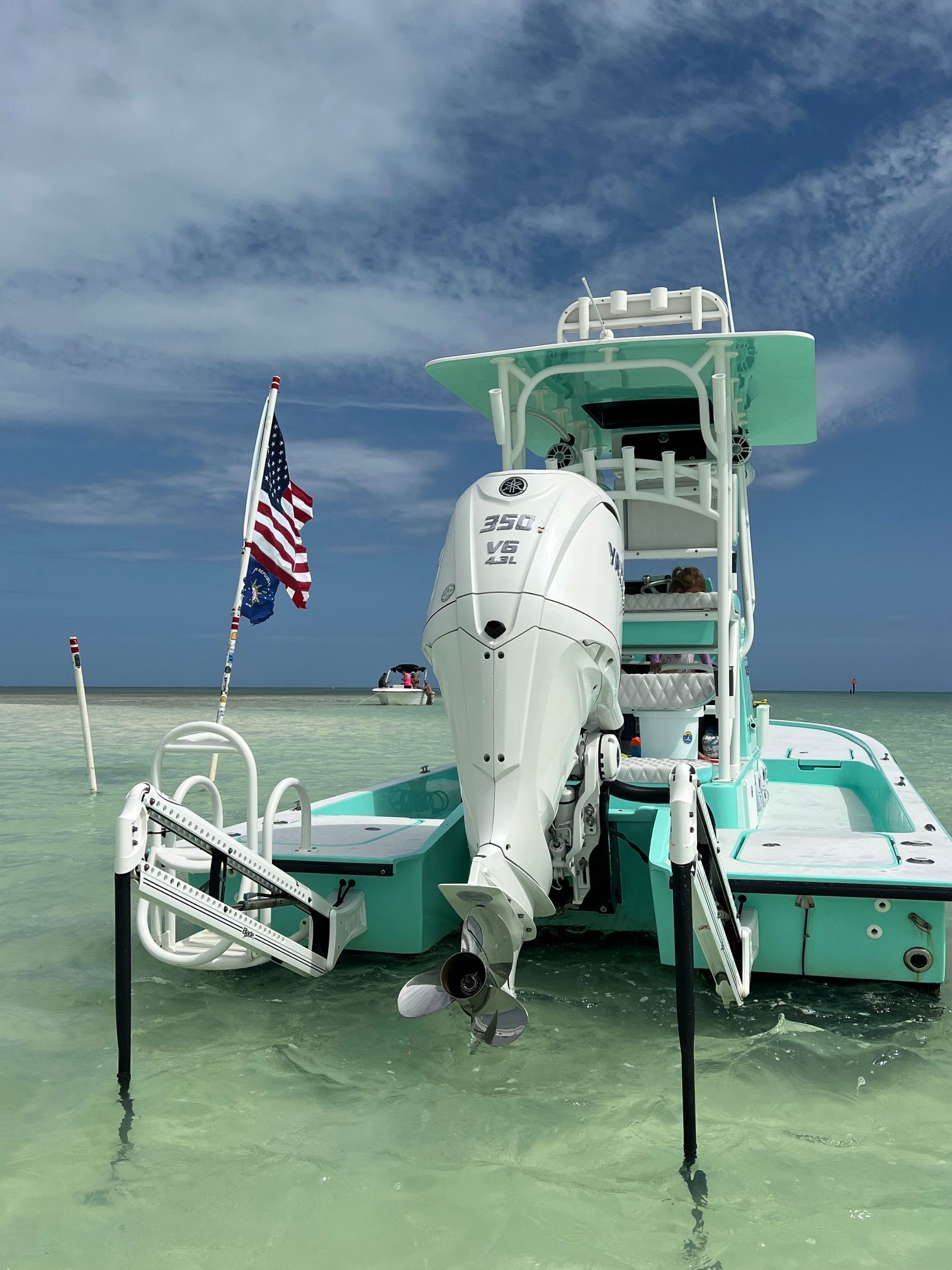 A turquoise boat with an outboard motor sits in shallow, clear water.