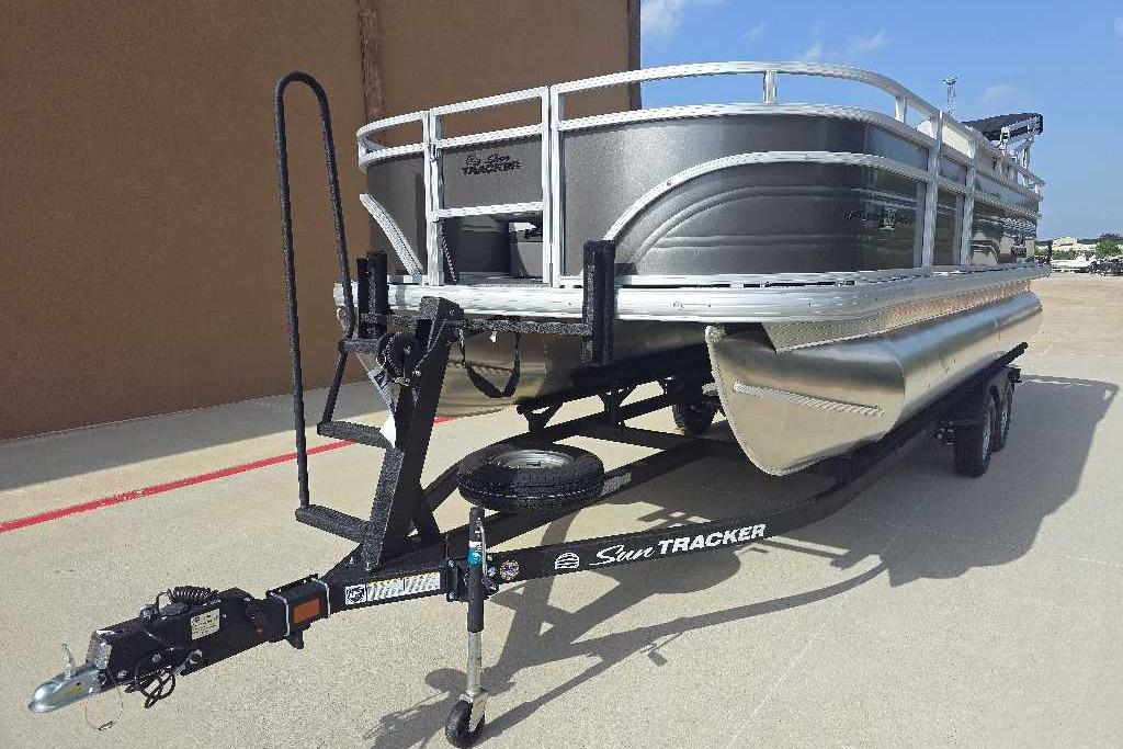 2026 Sun Tracker Fishin' Barge 20 DLX pontoon boat on trailer, parked outdoors.