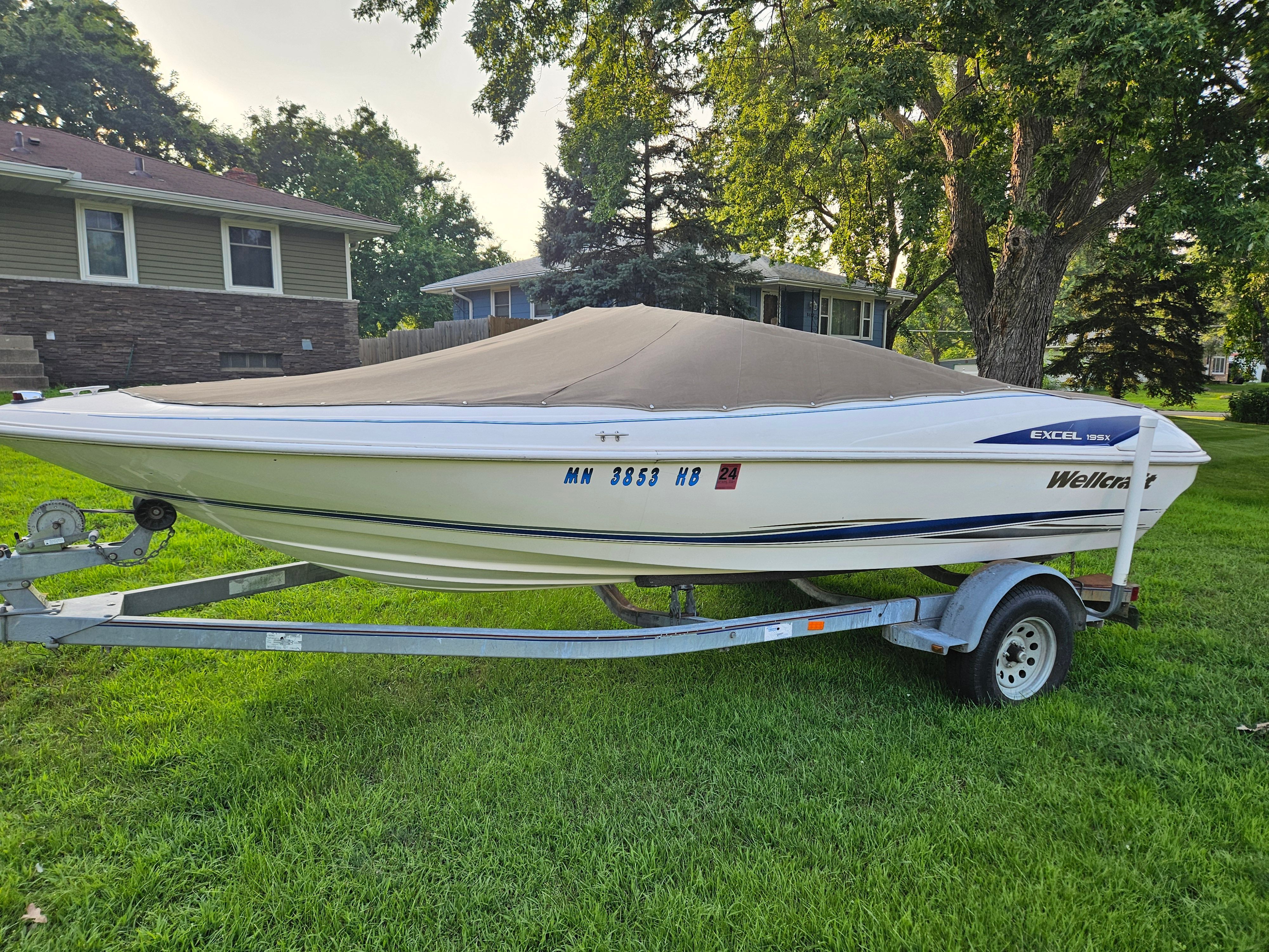 A 1996 Wellcraft Excel boat on a trailer, parked on a green lawn.