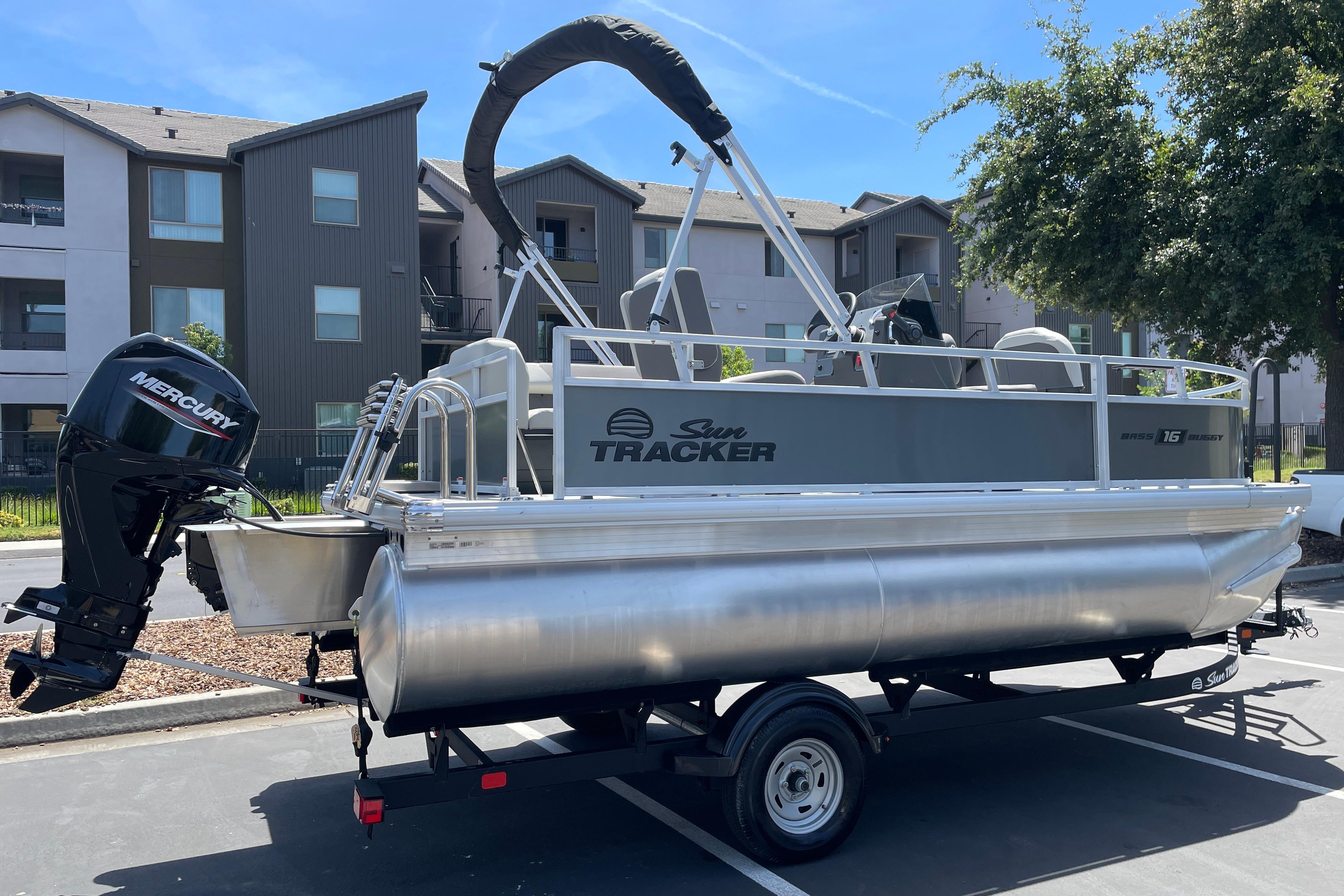 A Sun Tracker Bass Buggy 16 XL Select pontoon boat on a trailer in a residential area.