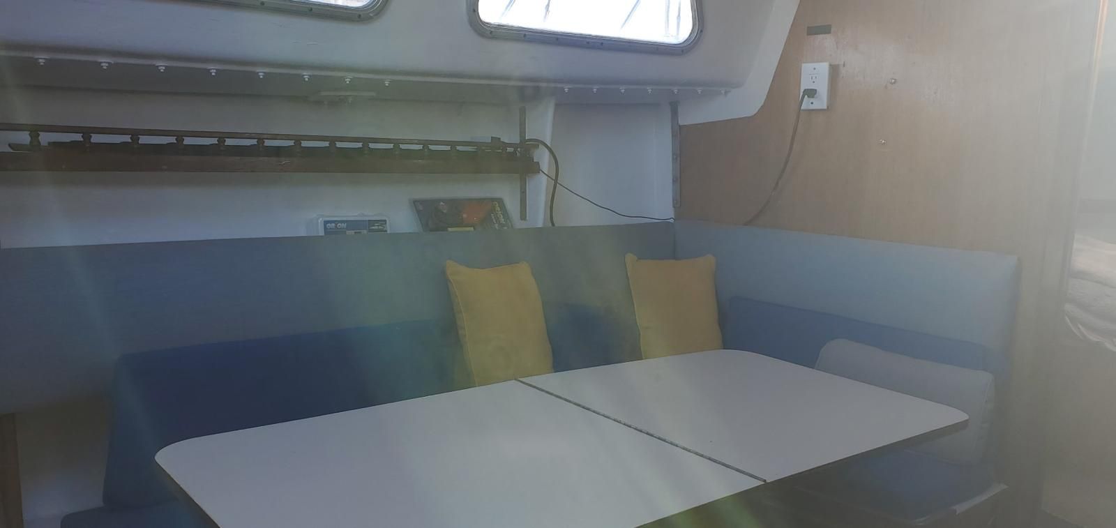 Interior of a boat with blue seating and yellow cushions, table in the center.