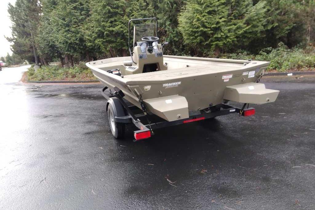 2026 Tracker Grizzly 1860 CC boat on trailer, parked on wet pavement near trees.